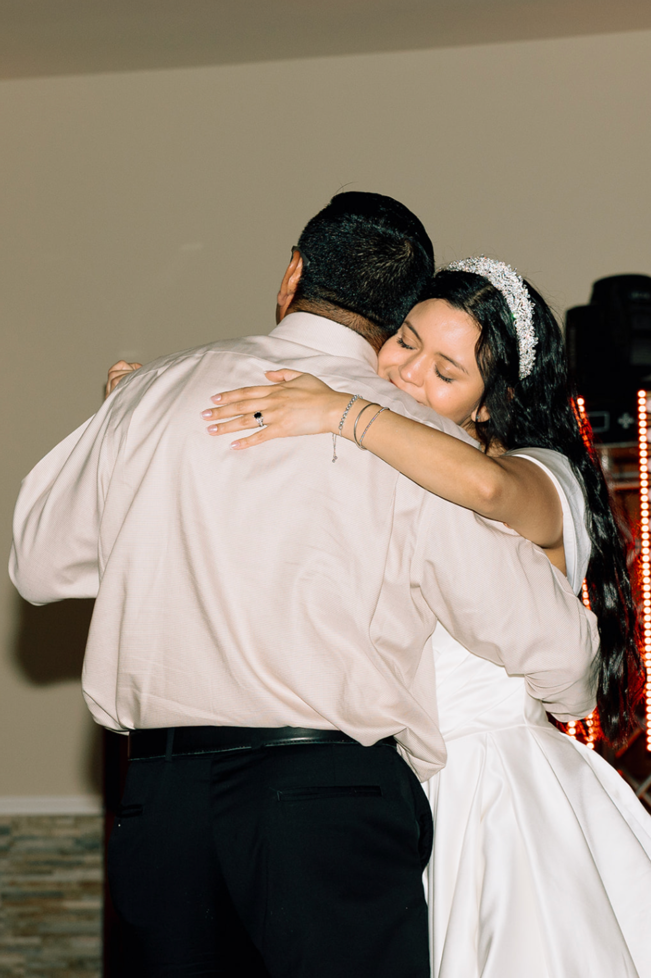 A couple sharing a dance at their wedding, with the woman embracing the man and resting her head on his shoulder.