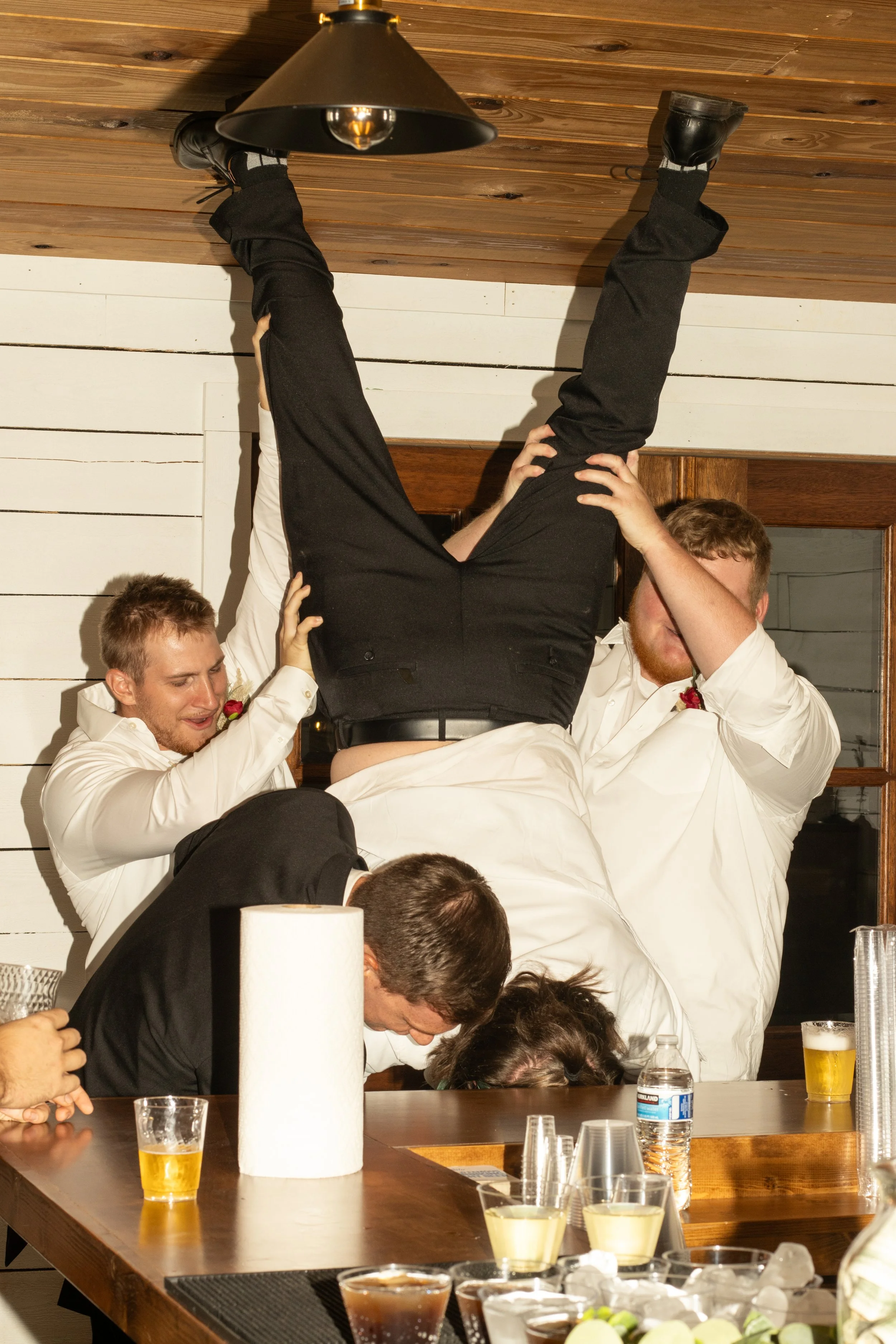 People at a celebration, with one person upside down and others supporting him.