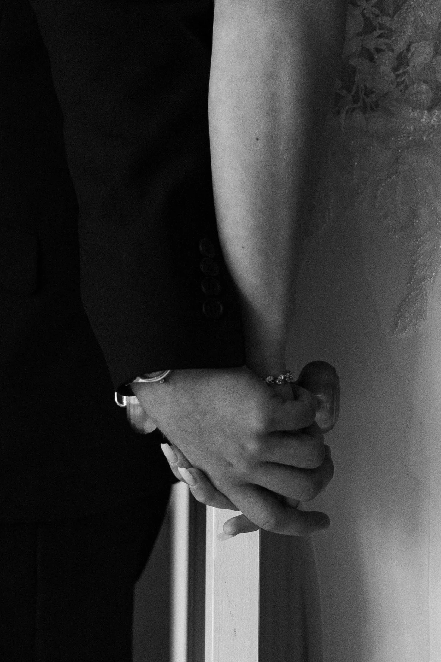 Close-up of two hands clasped together, one dressed in a formal suit and the other with a tattoo on the arm, with a background of blurred leaves.