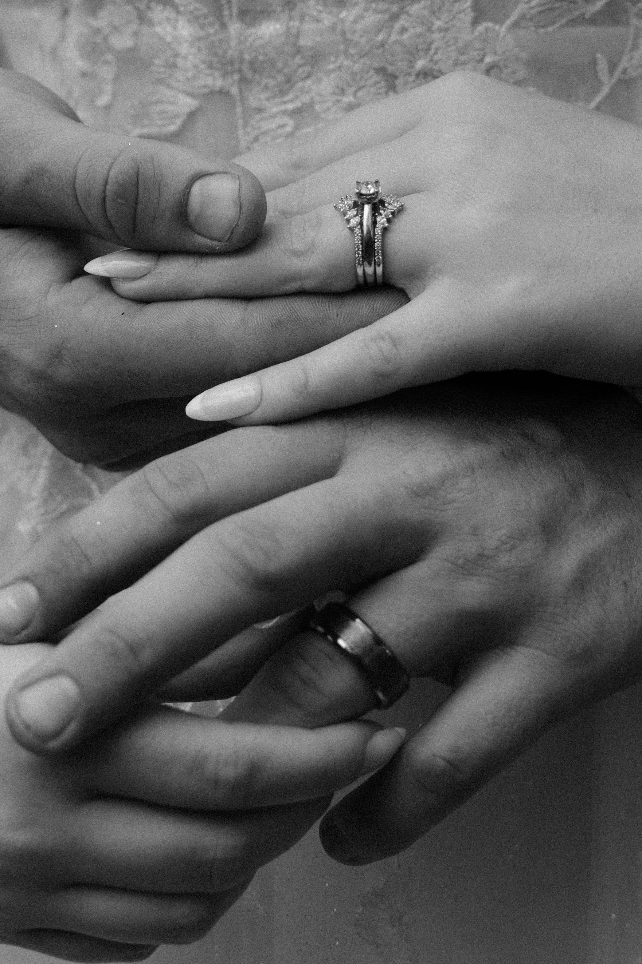 Multiple hands, each wearing a ring, gently placed on top of each other, some hands with light skin and others with dark skin, with a focus on the rings and the connection between the hands.