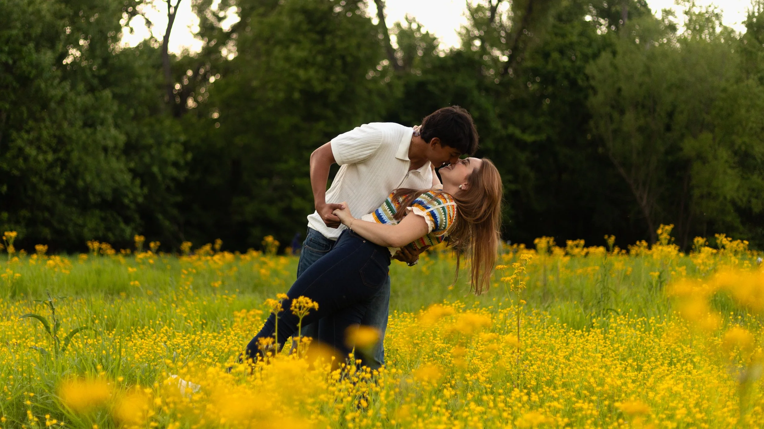 A couple dancing in a field of yellow flowers with trees in the background.