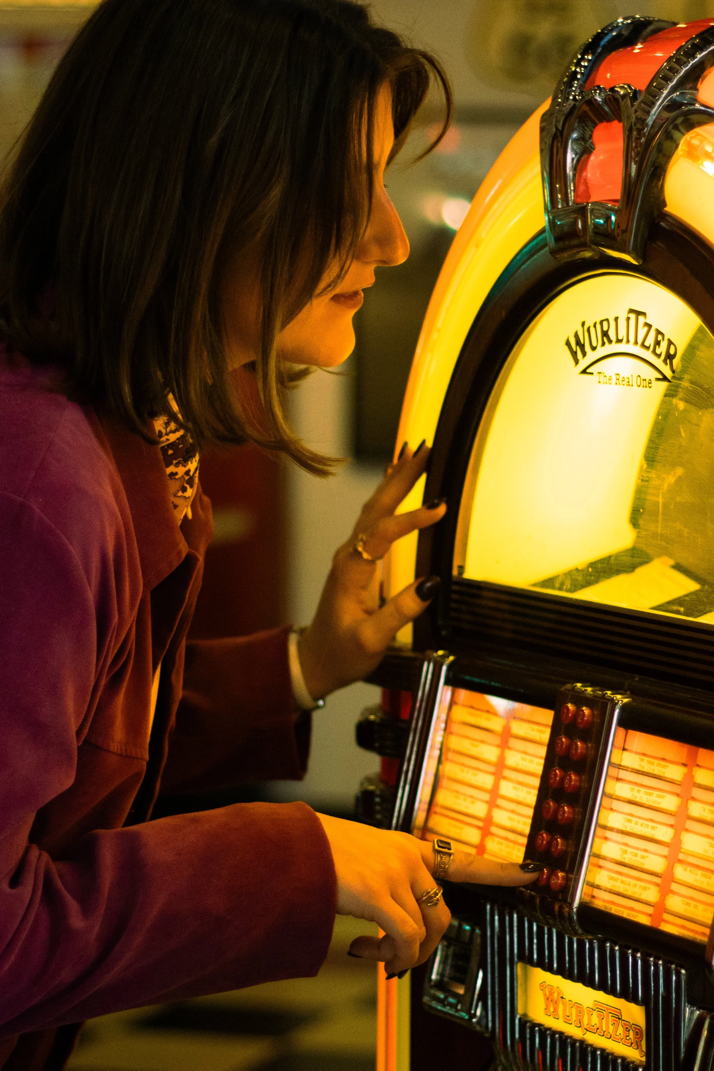 Woman playing a vintage Wurlitzer jukebox in a dimly lit setting.