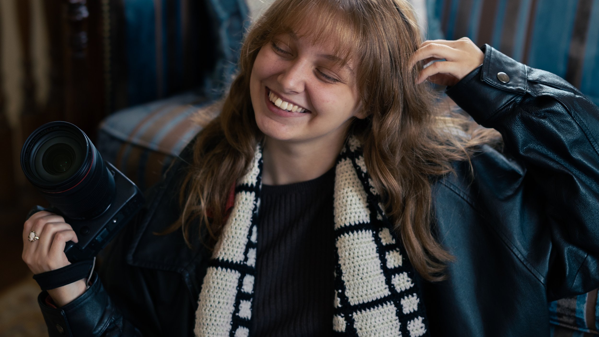 A woman with brown hair and a black leather jacket smiling while holding a camera.