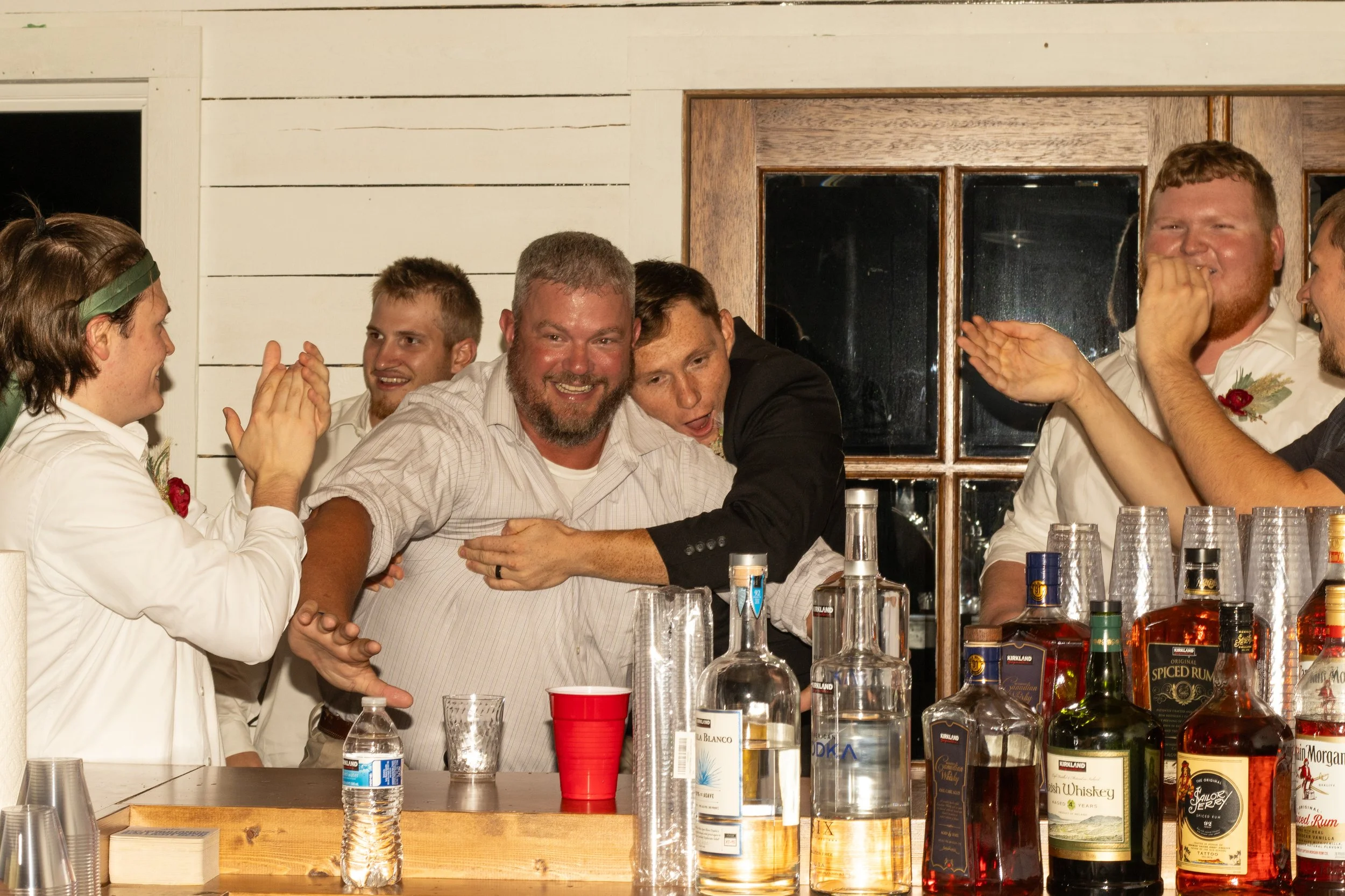 A group of men sharing a joyful moment at a party, with drinks and bottles on the table in front of them, celebrating and laughing.