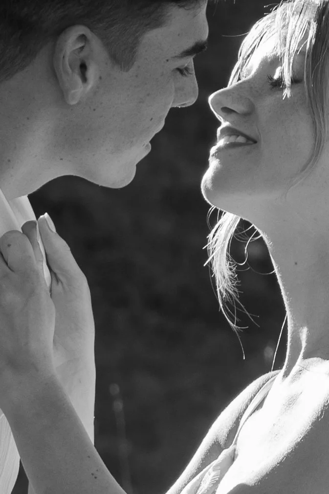A black and white photo of a couple close together, with the man gently holding the woman's neck while they look into each other's eyes.