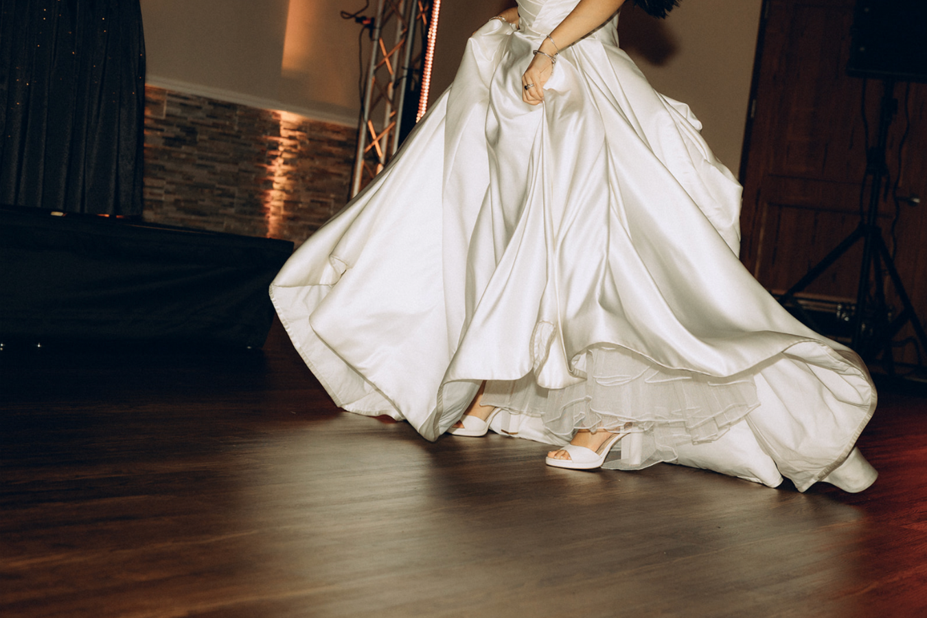 Bride in a white wedding gown and white high heels dancing on a wooden floor.