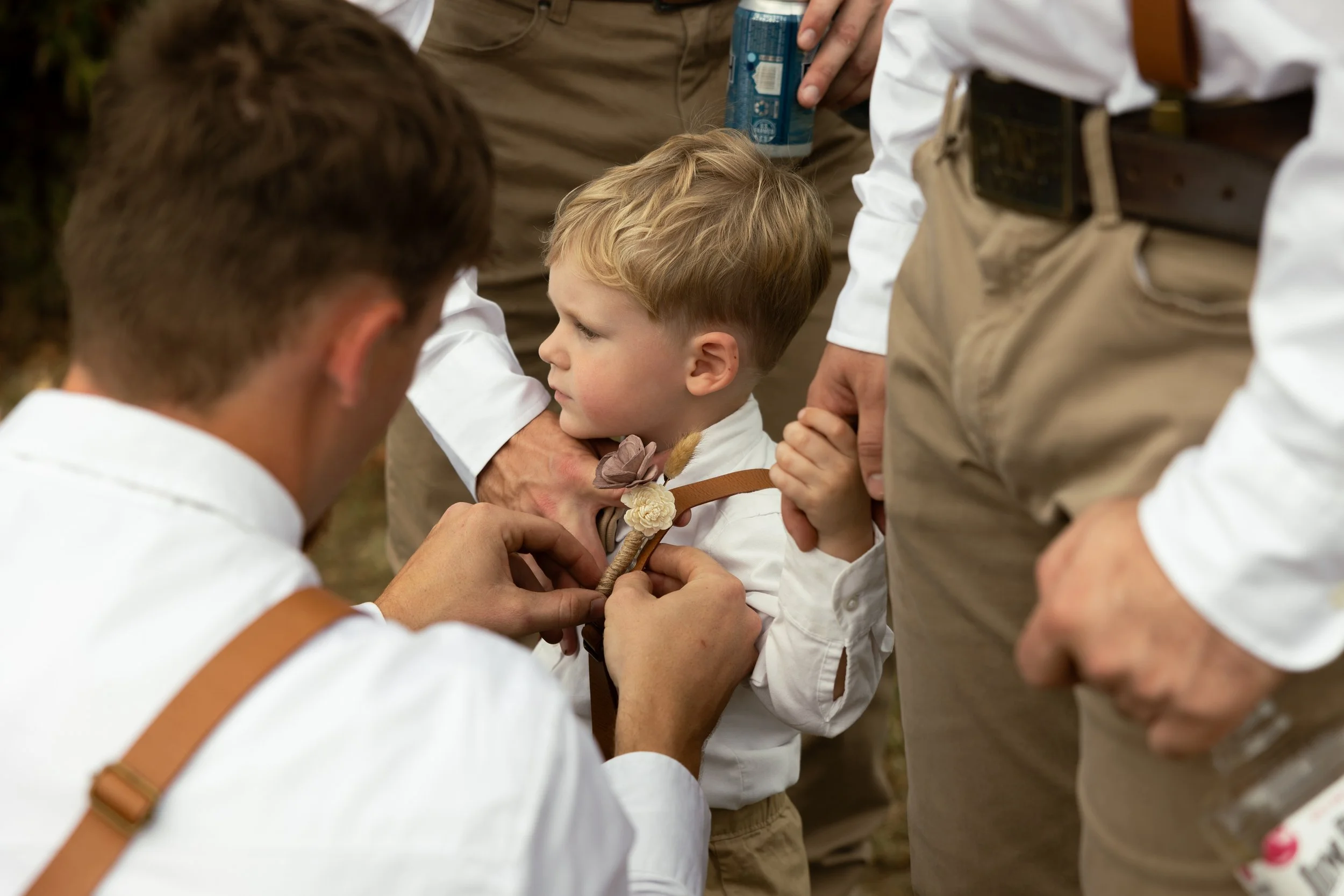 A young boy having a lei placed around his neck by an adult during a ceremony, with other adults around him.