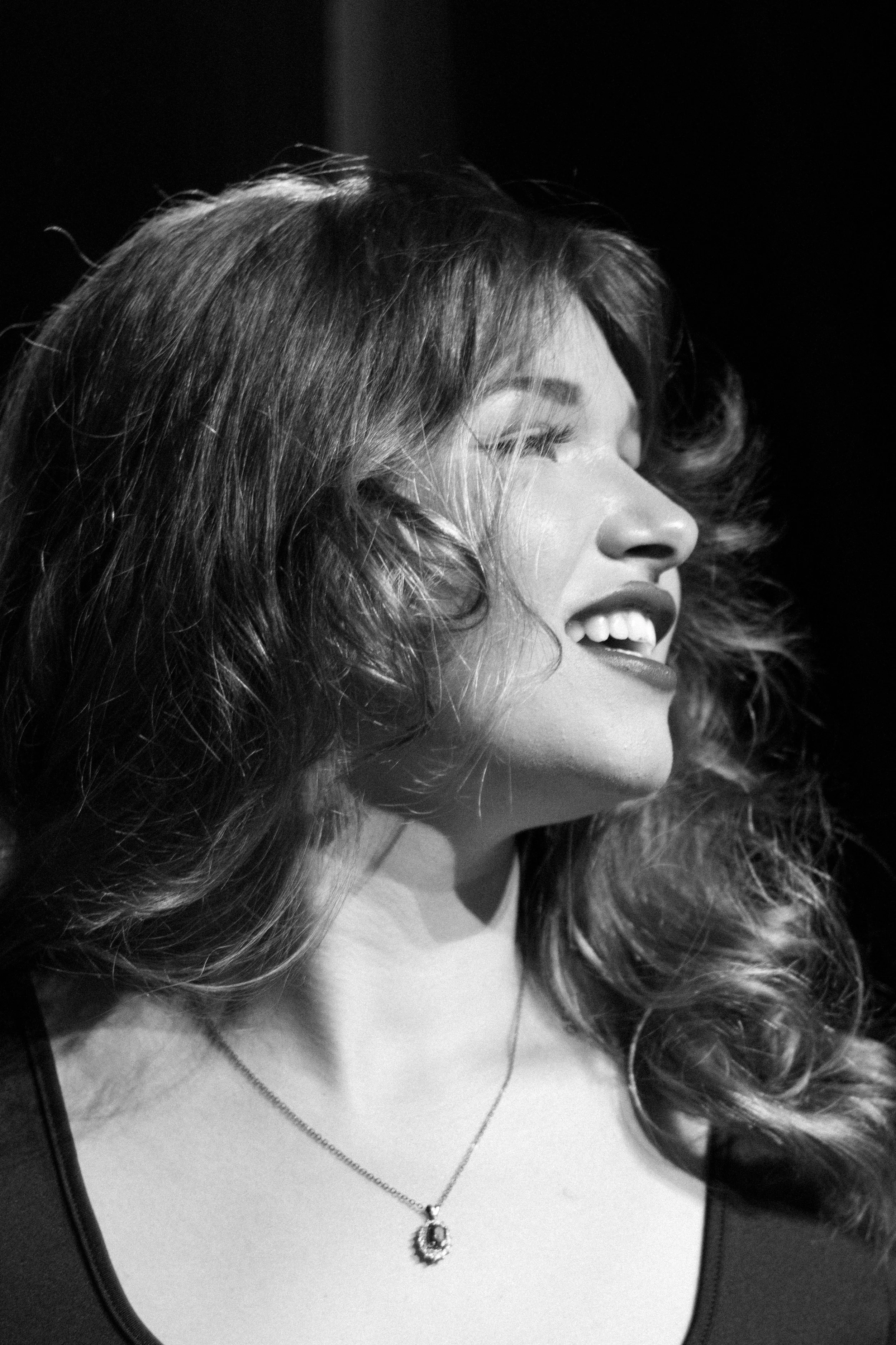 Black and white photo of a smiling woman with wavy hair, wearing a necklace.