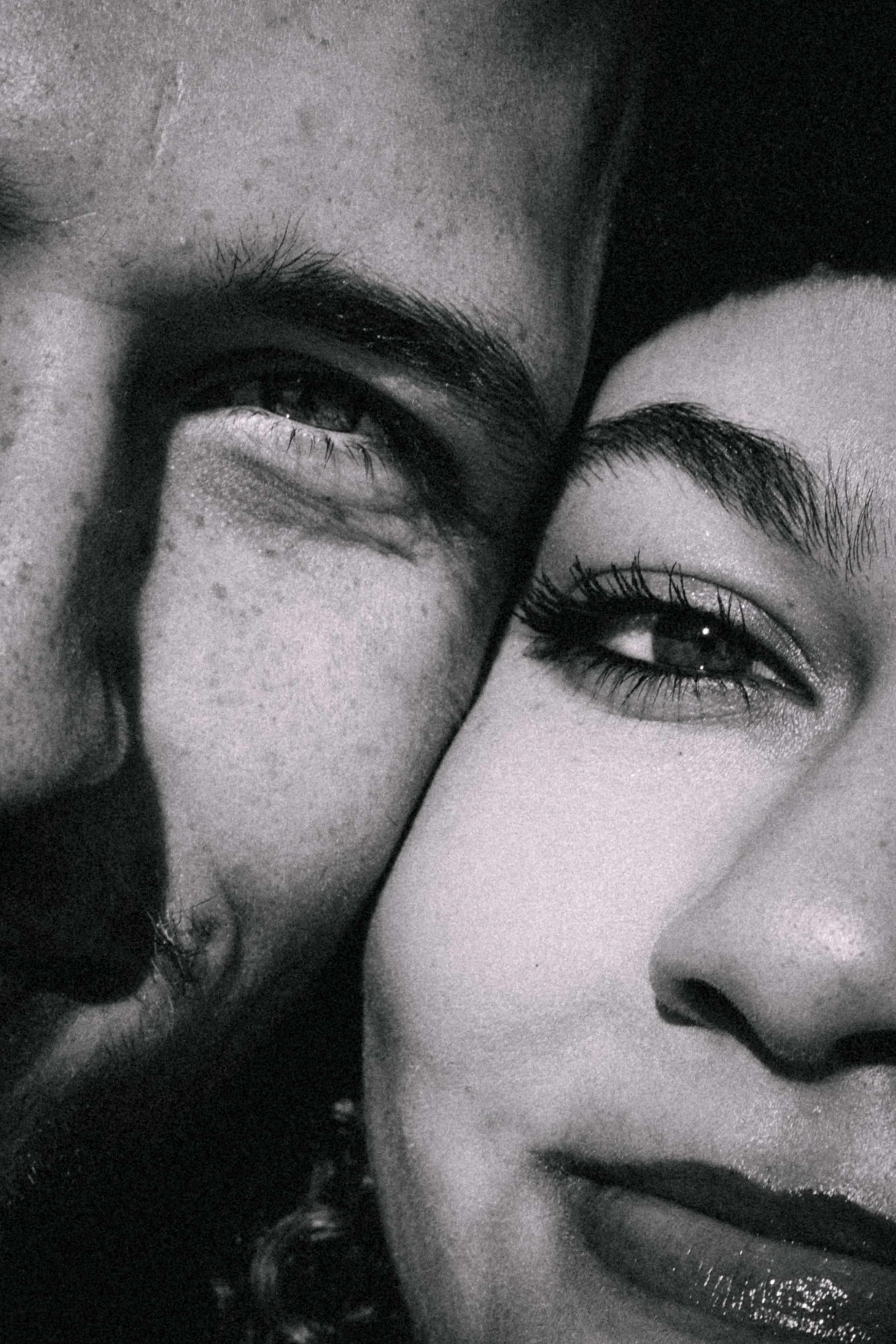 Close-up of two people with their faces very close, showing their eyes and part of their noses and mouths, in black and white.