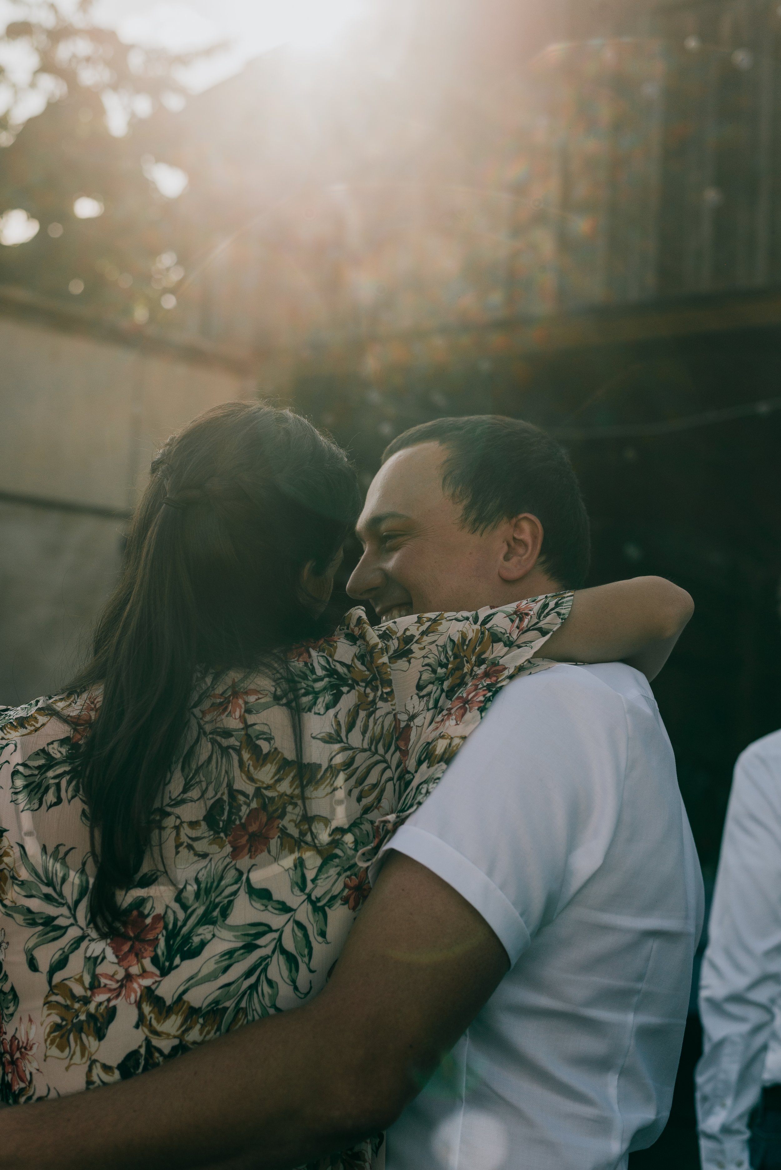 A couple hugging outdoors, smiling, with sunlight shining behind them at an Italian destination wedding.
