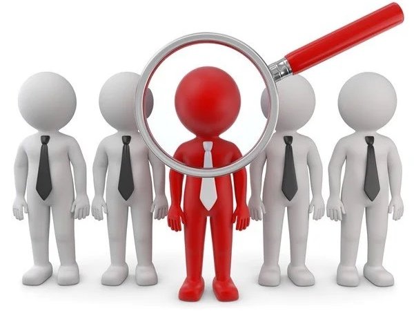 Ein rotes Männchen in Anzug mit Lupe untersucht eine Gruppe weißer Männchen in Anzügen, alle ohne Gesicht, symbolisiert Personalauswahl.