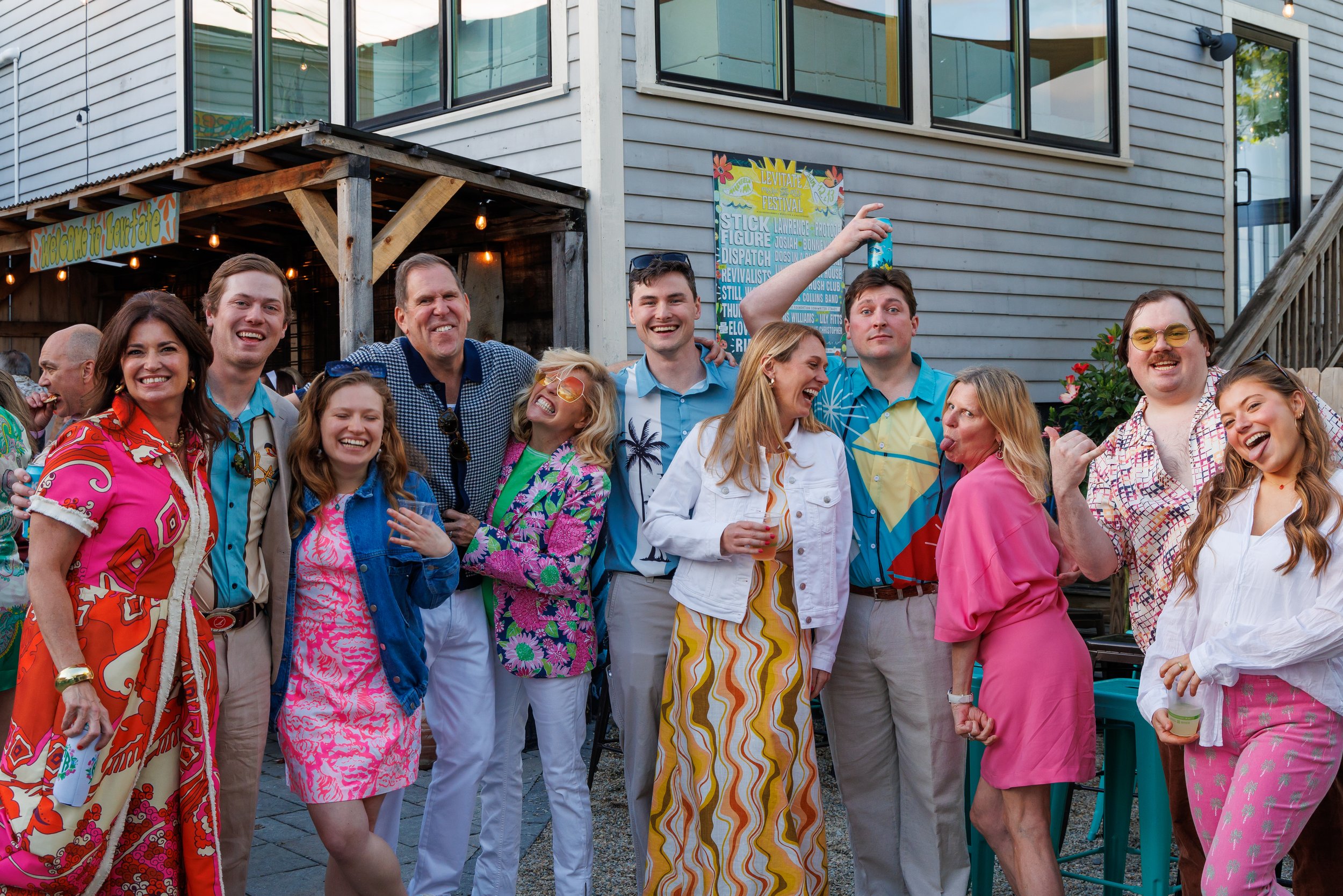 A group of people enjoying a party outdoors in colorful, retro clothing, standing in front Levitate Backyard in Marshfield, MA