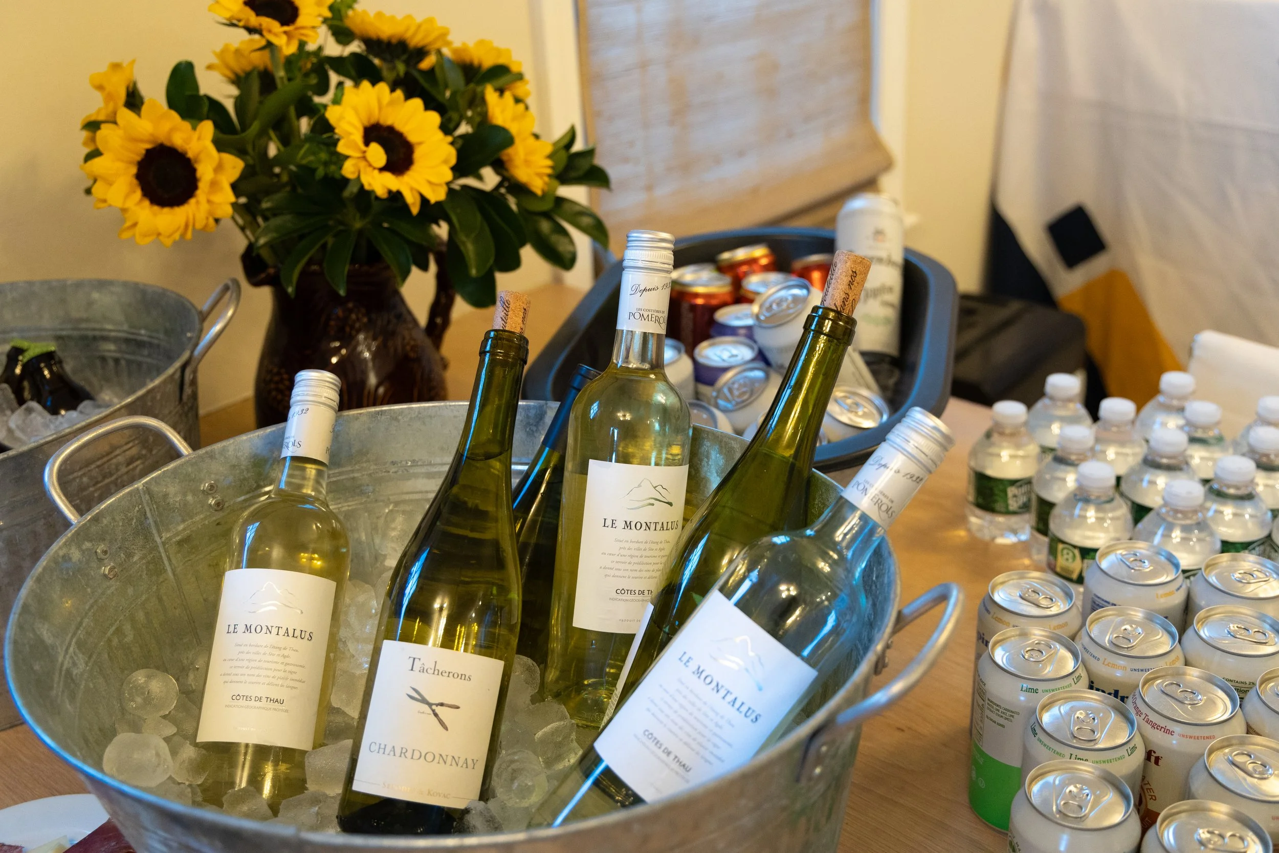 Bottles of white wine in ice-filled metal container, with sunflower bouquet and canned drinks in the background. Shot at a Corporate Event in Manchester, New Hampshire.