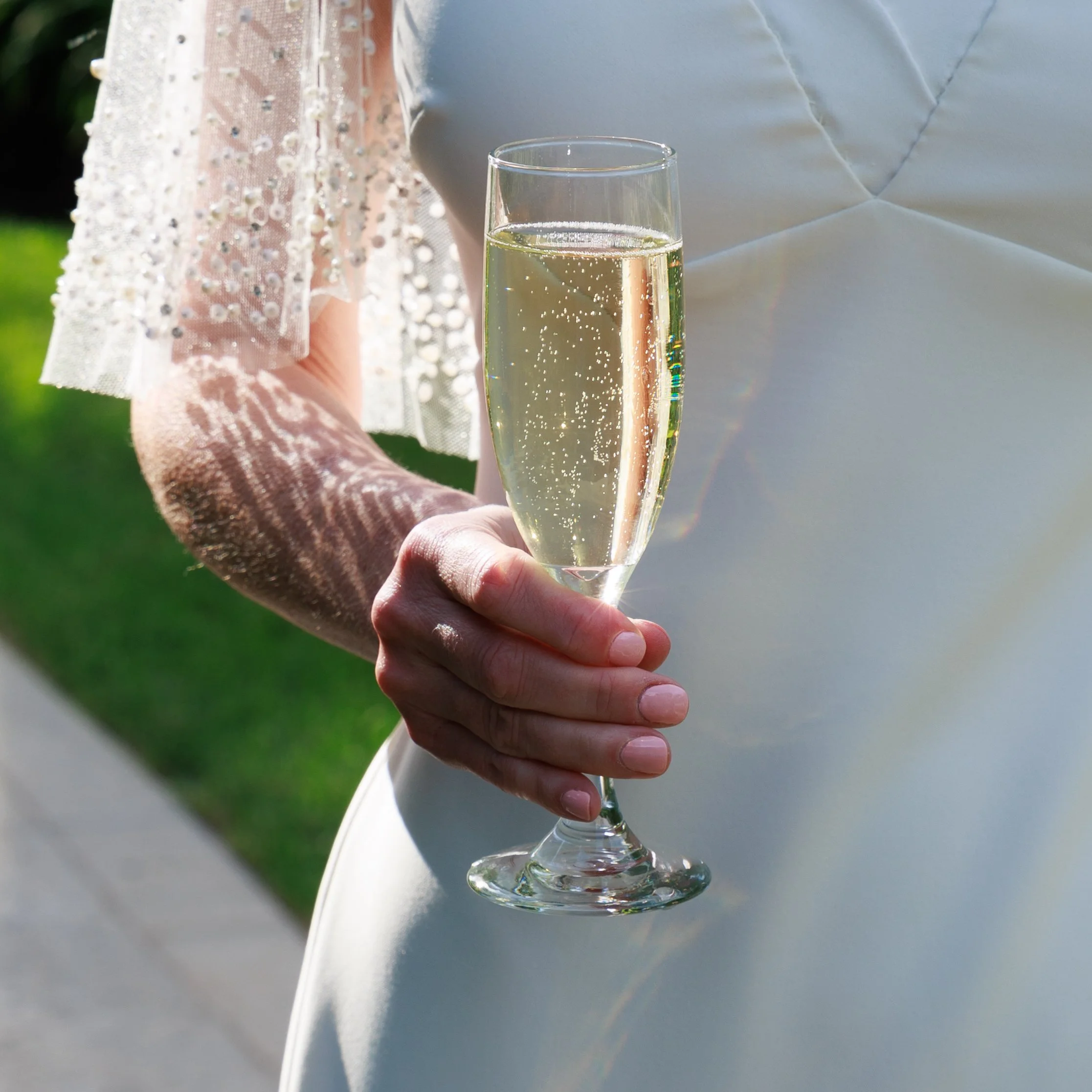 A bride in a white dress holding a glass of champagne outdoors in daylight. Shot at Briar Barn Inn in Rowley, Massachusetts.