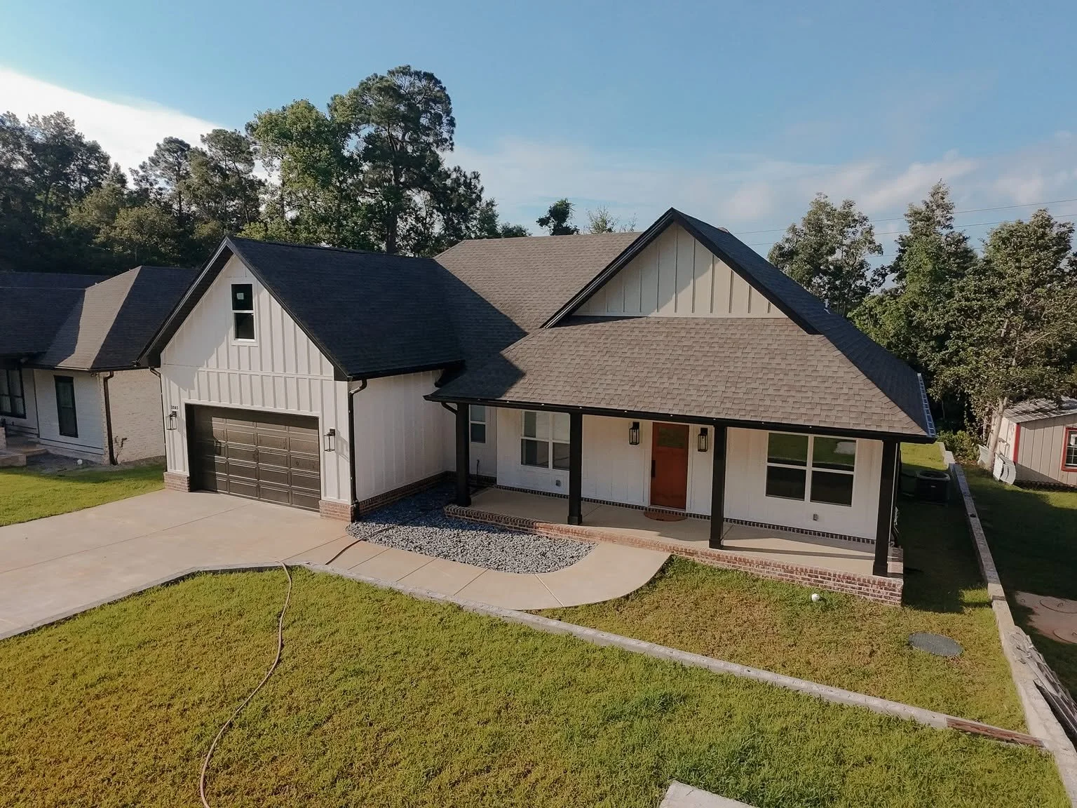 A newly completed custom home in Northwest Florida, featuring white board-and-batten siding, a covered front porch, black garage doors, and a thoughtfully designed layout built for comfortable family living.