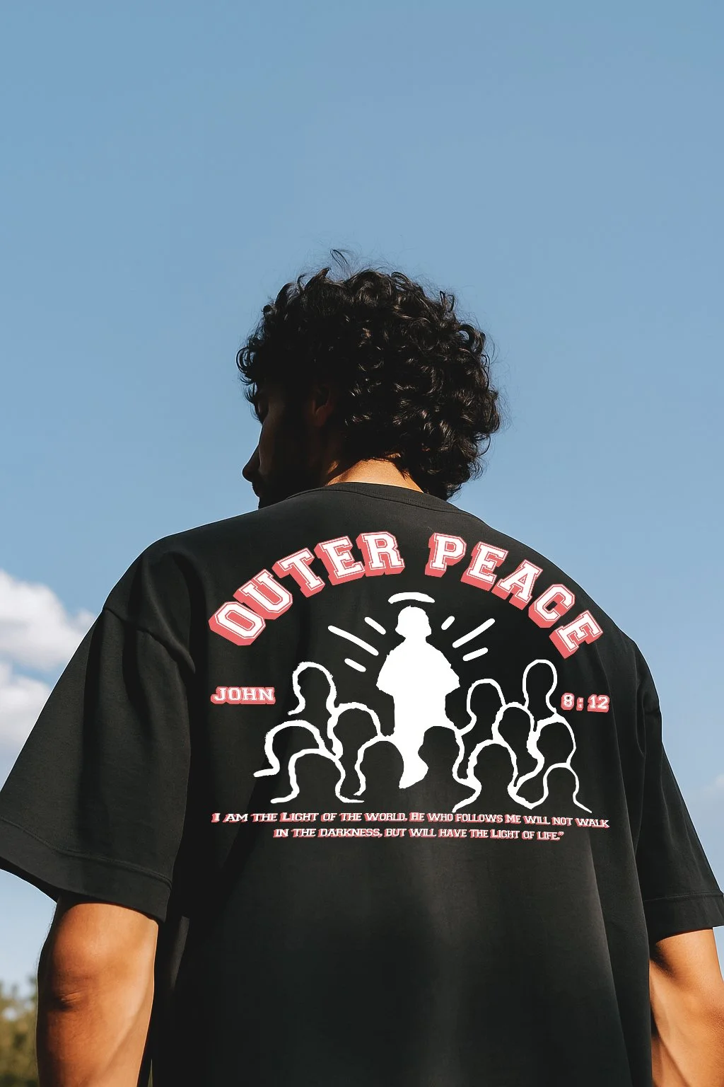 Back of a person wearing a black t-shirt with a graphic and text, standing outdoors against a blue sky with some clouds.