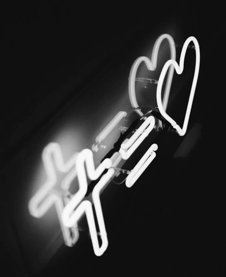 A neon sign featuring a hand making a peace sign with two fingers and a heart shape, illuminated in white against a dark background.
