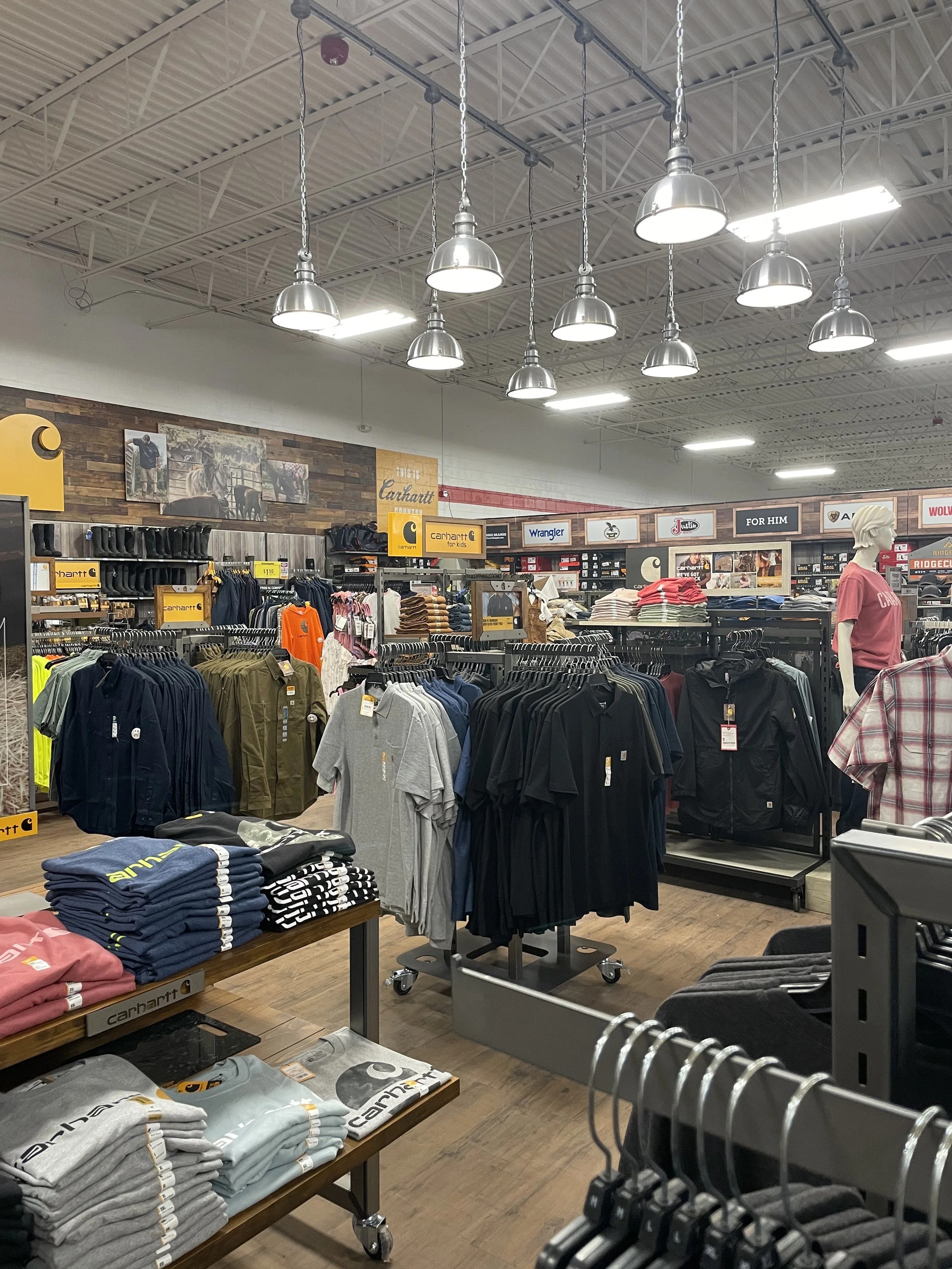 Inside a retail clothing store displaying various apparel, including shirts, jackets, and folded clothes, with signs and mannequins.