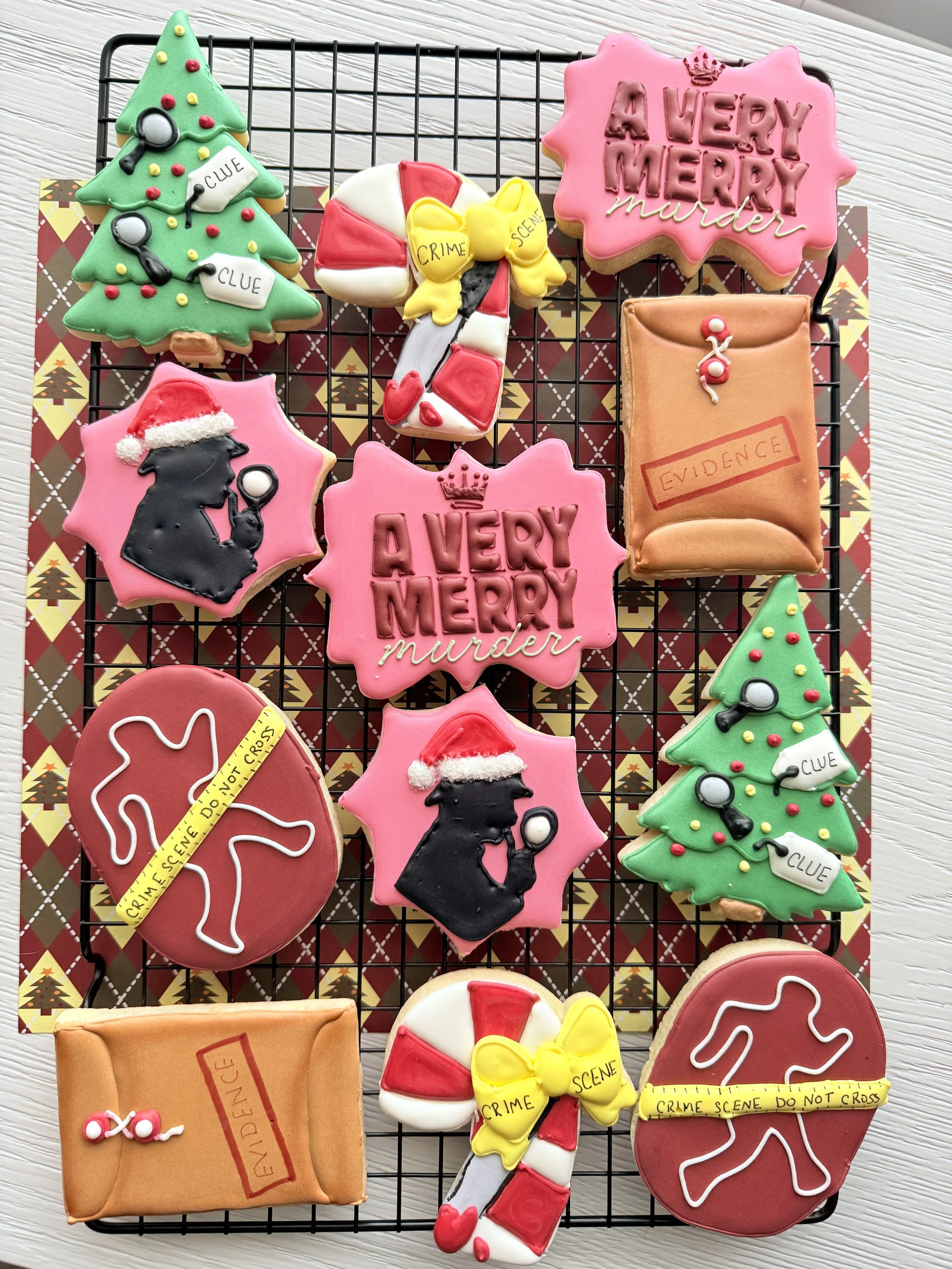 Cookies decorated with Christmas and crime scene themes, including a Christmas tree with 'clue' tags, a candy cane with 'crime' and 'scene' tags, silhouettes of detectives with Santa hats, an evidence envelope, and cookies with the phrase 'A Very Mer