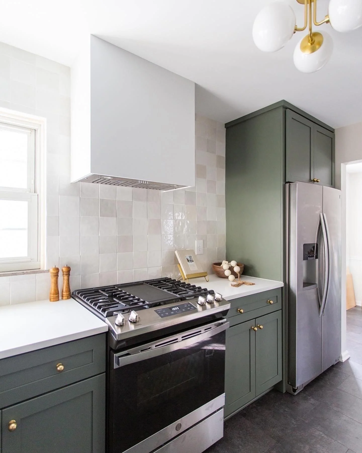 Modern kitchen with green cabinets, stainless steel stove and refrigerator, white countertops, and a gold and white ceiling light