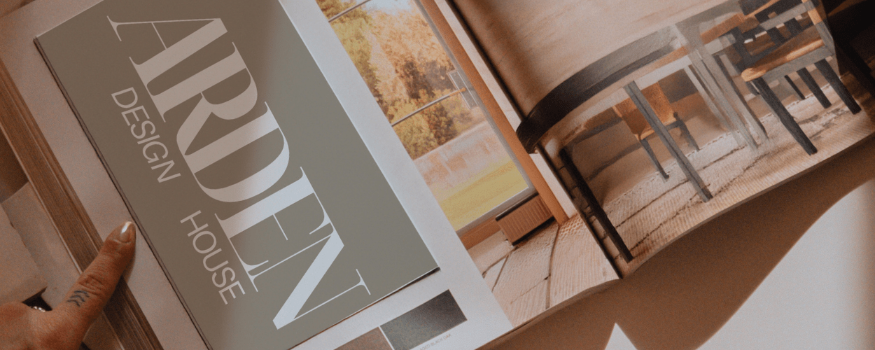 Open home design magazine showing a room with wooden flooring, large windows, and dining table with chairs.