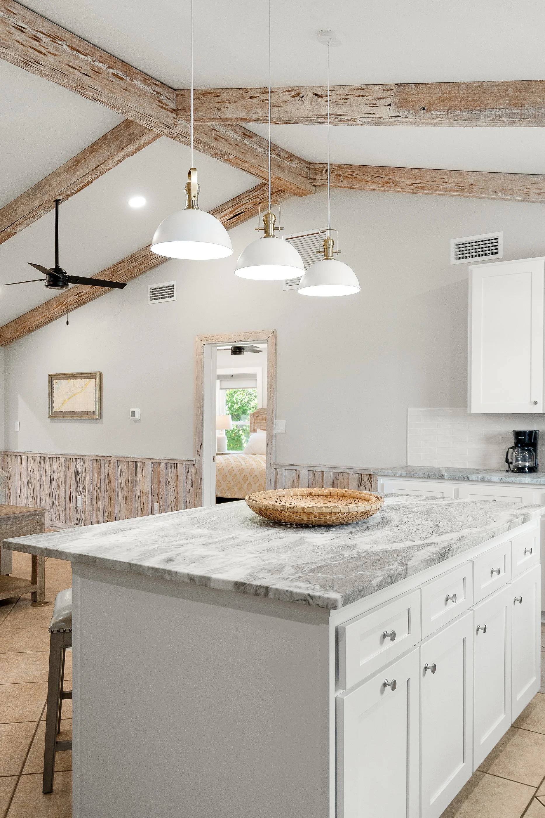 Kitchen with white cabinets, marble countertop, wooden beams on ceiling, and pendant lights.