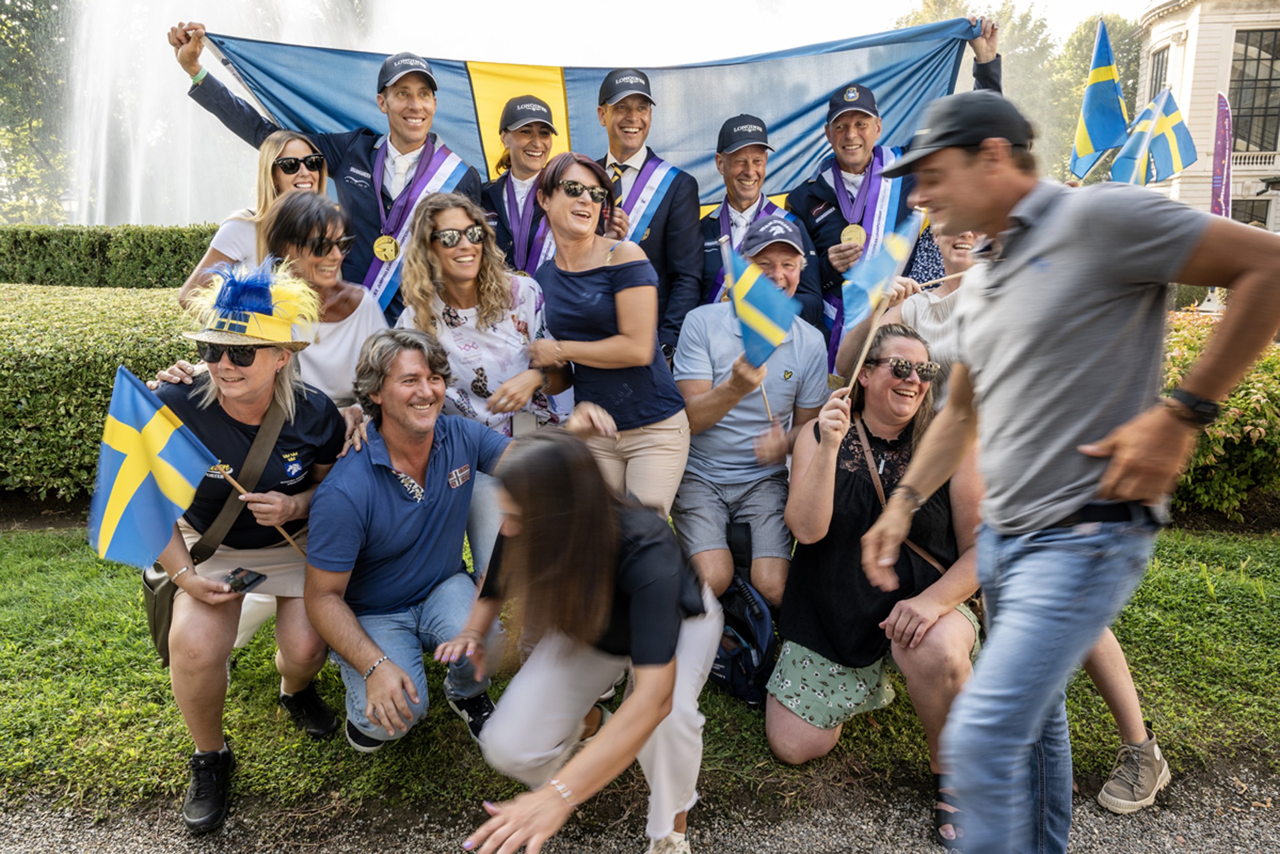 När det svenska guldlaget ställer upp för att fotograferas med flaggan dyker de svenska fansen upp, de hoppar genast in i bilden och är på väldigt bra humör