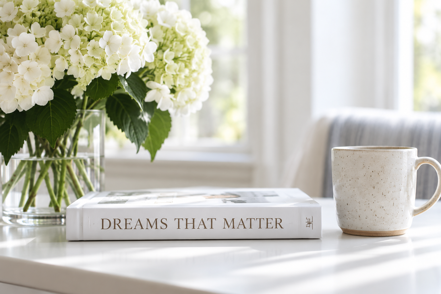 Dreams That Matter book by Jasmine Chambers beside white hydrangeas and a ceramic mug in a bright, sunlit room.