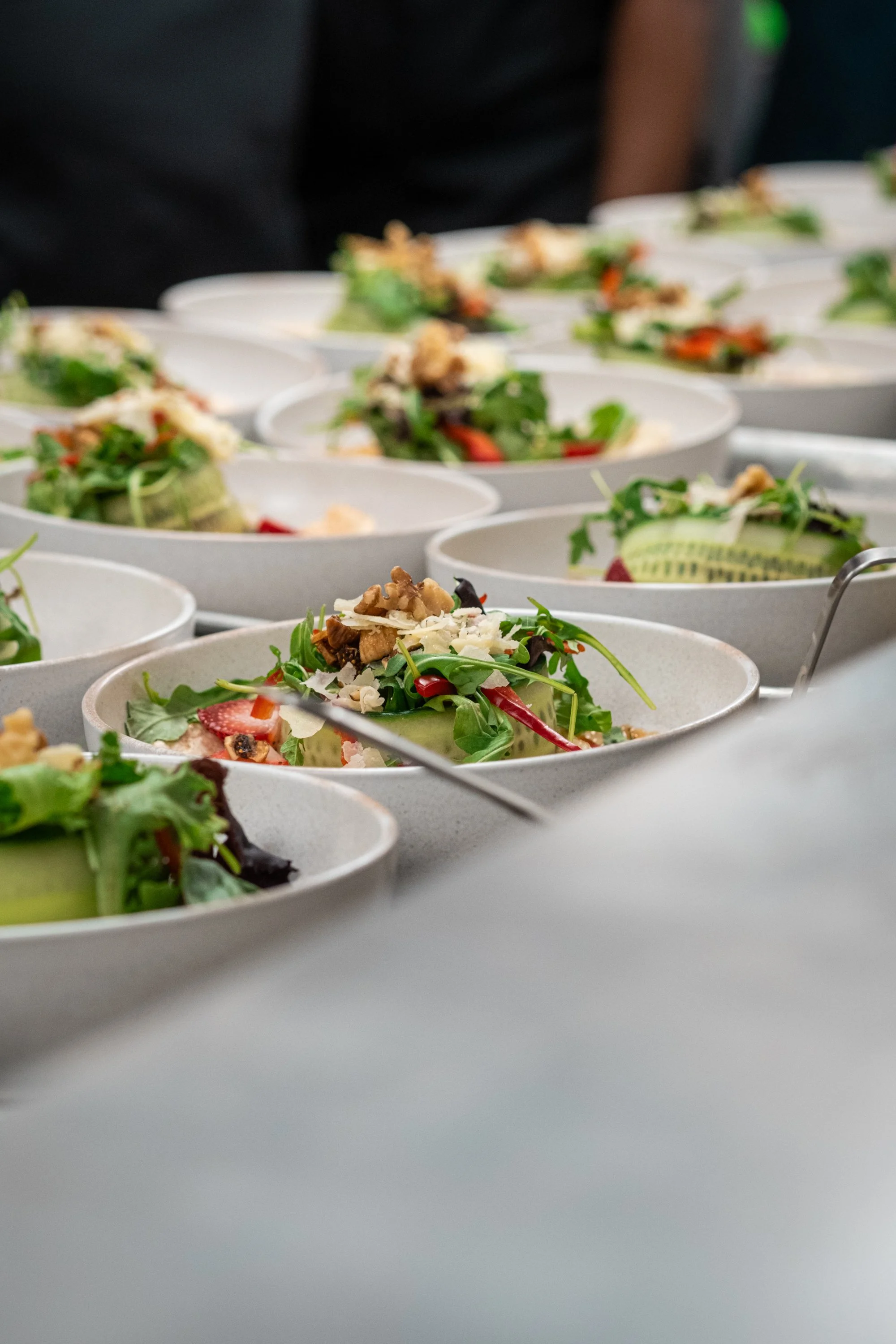 Multiple bowls of salad with greens, strawberries, nuts, cheese, and vegetables on a table, likely at a buffet or catered event.