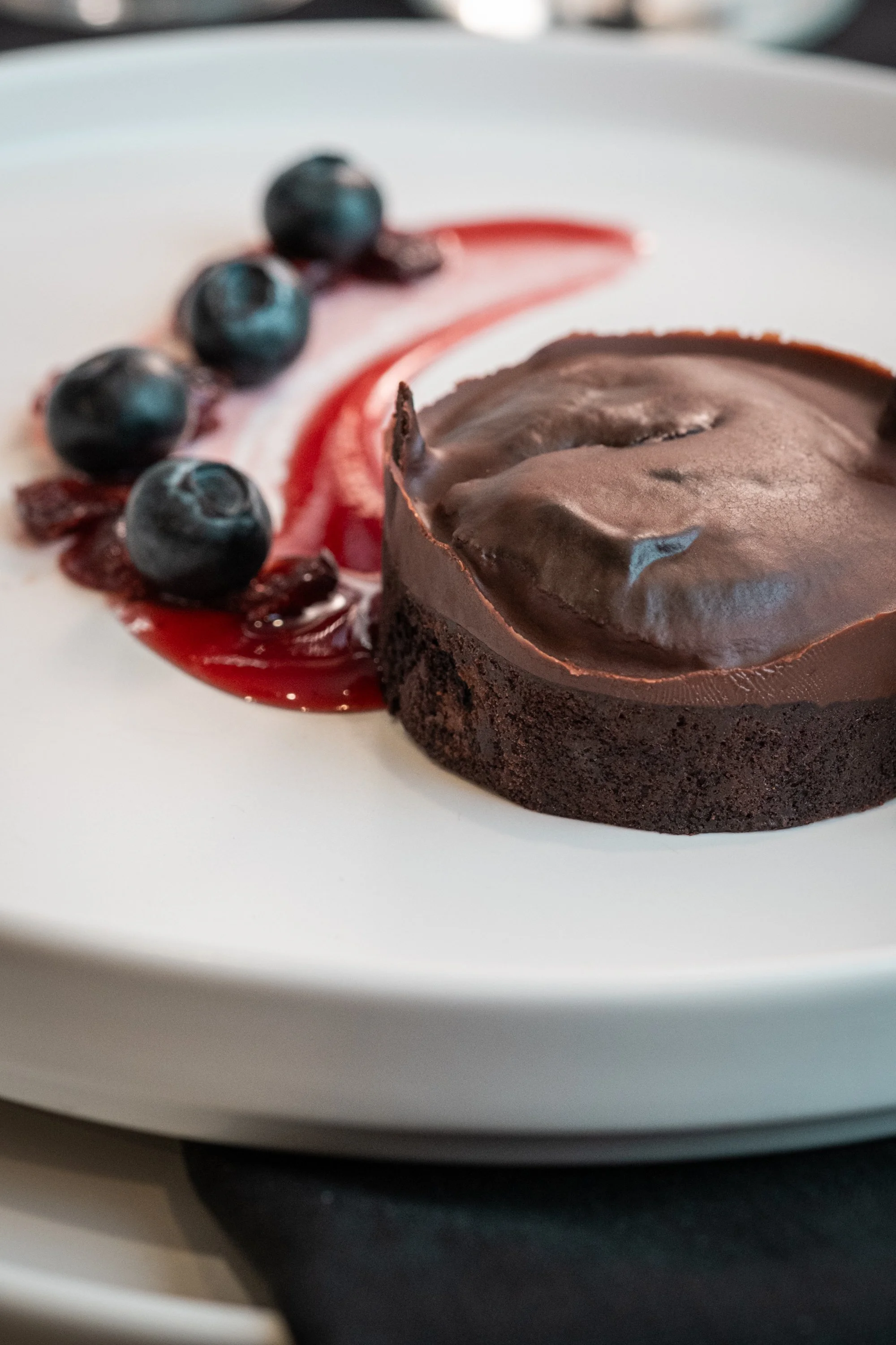 A close-up of a chocolate dessert with blueberries on a white plate.