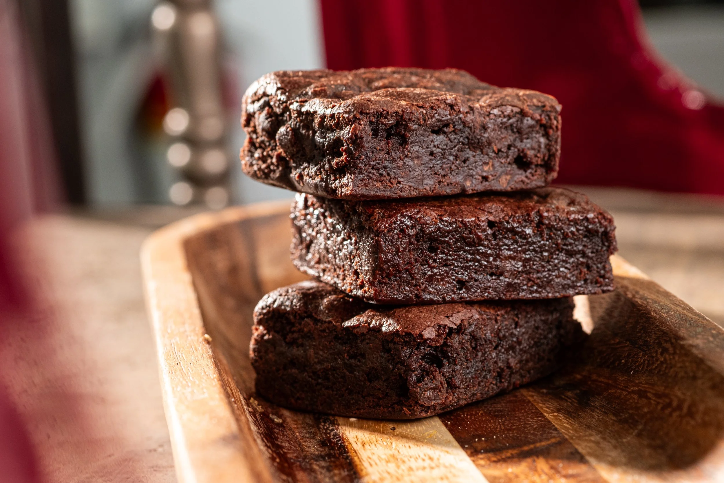 Stack of three dark chocolate brownies on a wooden tray.