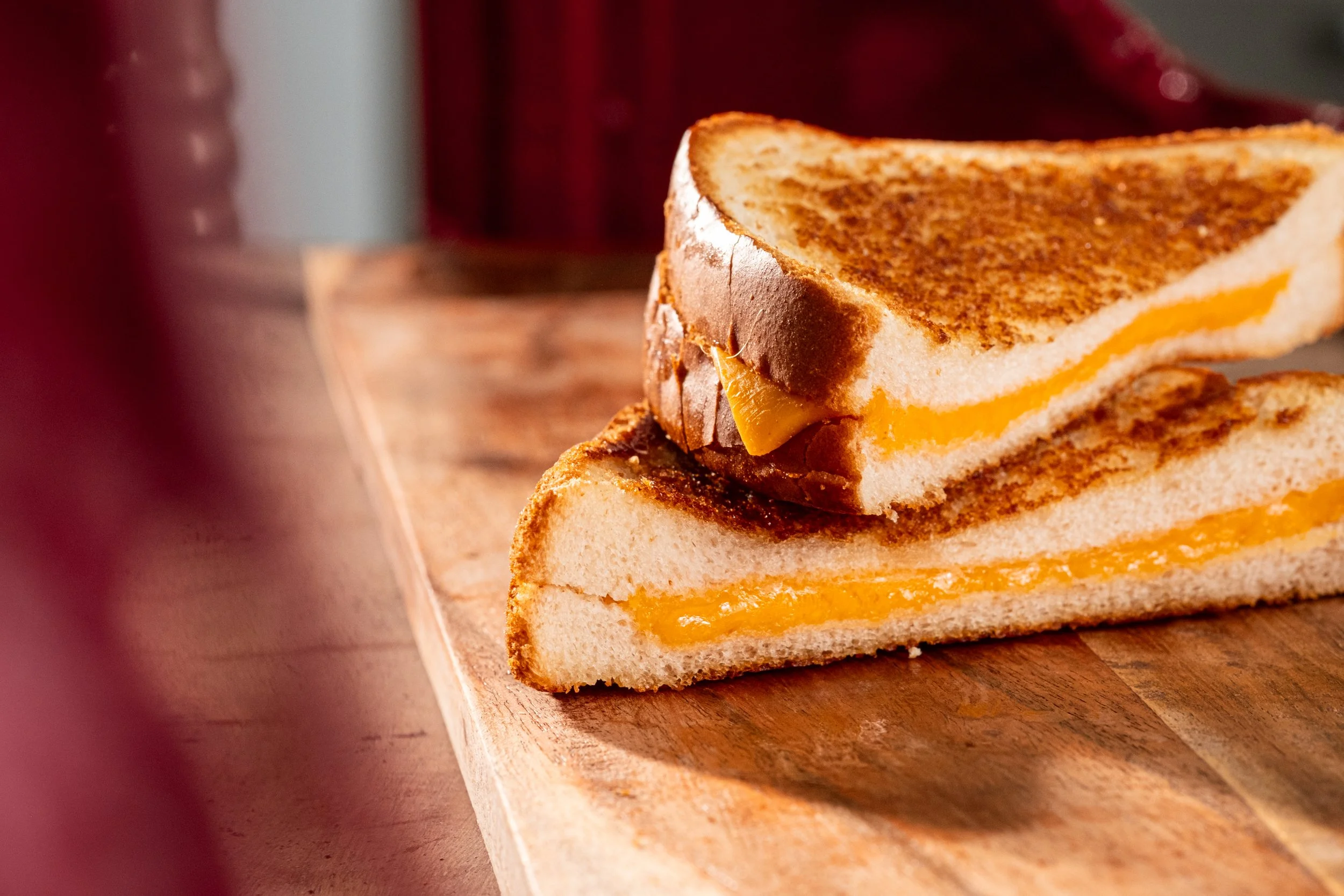 Close-up of two slices of grilled cheese sandwiches on a wooden surface, with melted cheese inside.