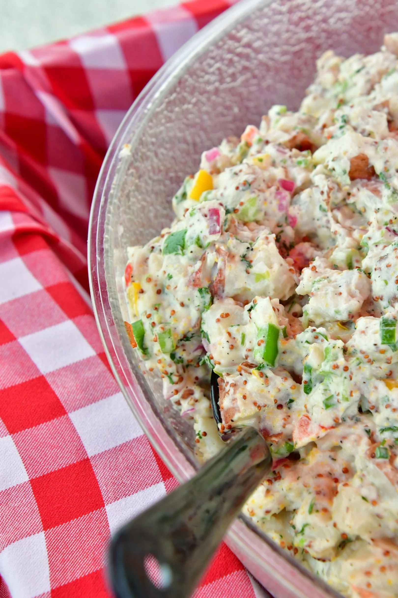 A bowl of a creamy mini red potato salad, served in a clear dish on a red and white checkered tablecloth.