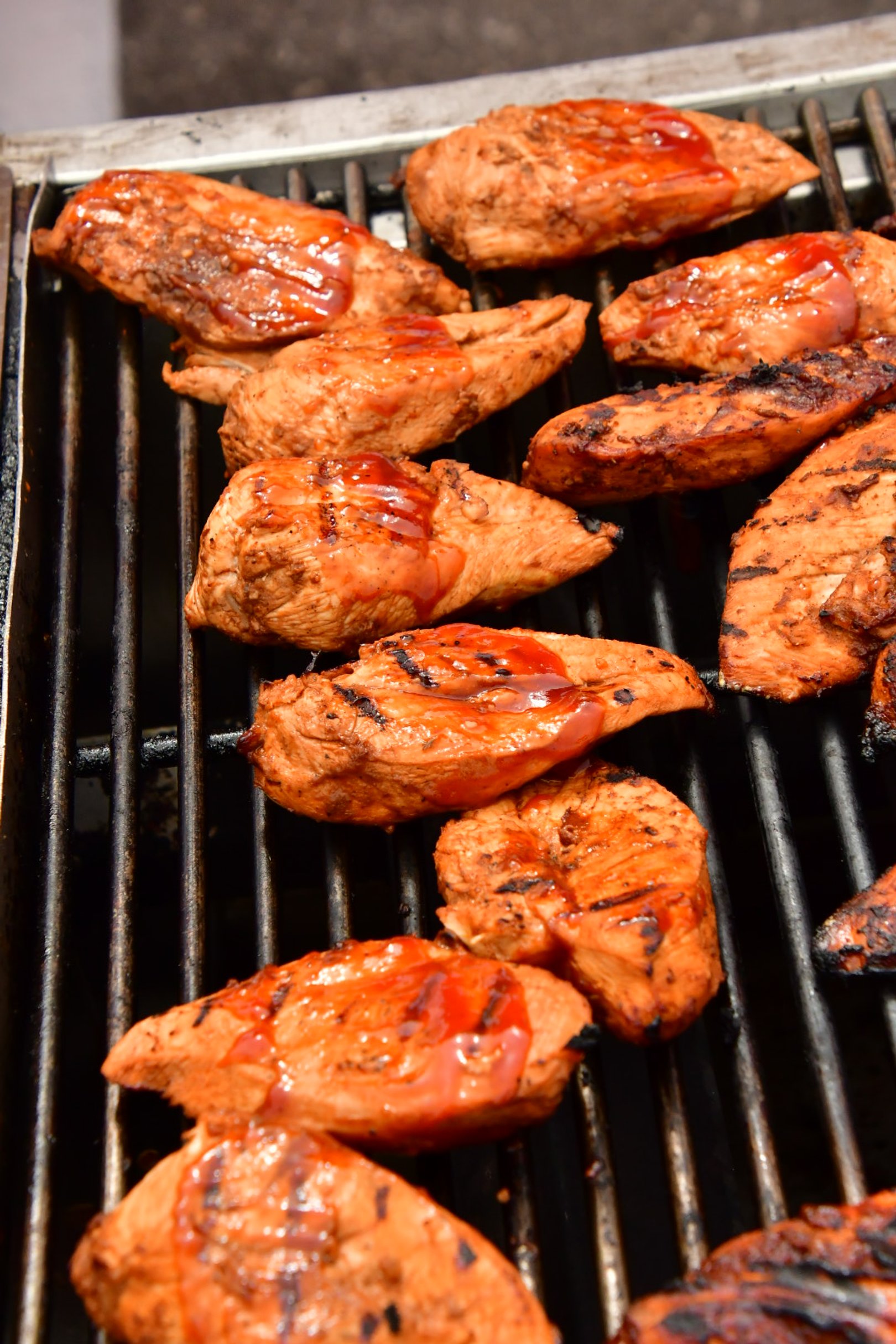 Boneless chicken breasts grilled on a barbecue, smothered in barbecue sauce.