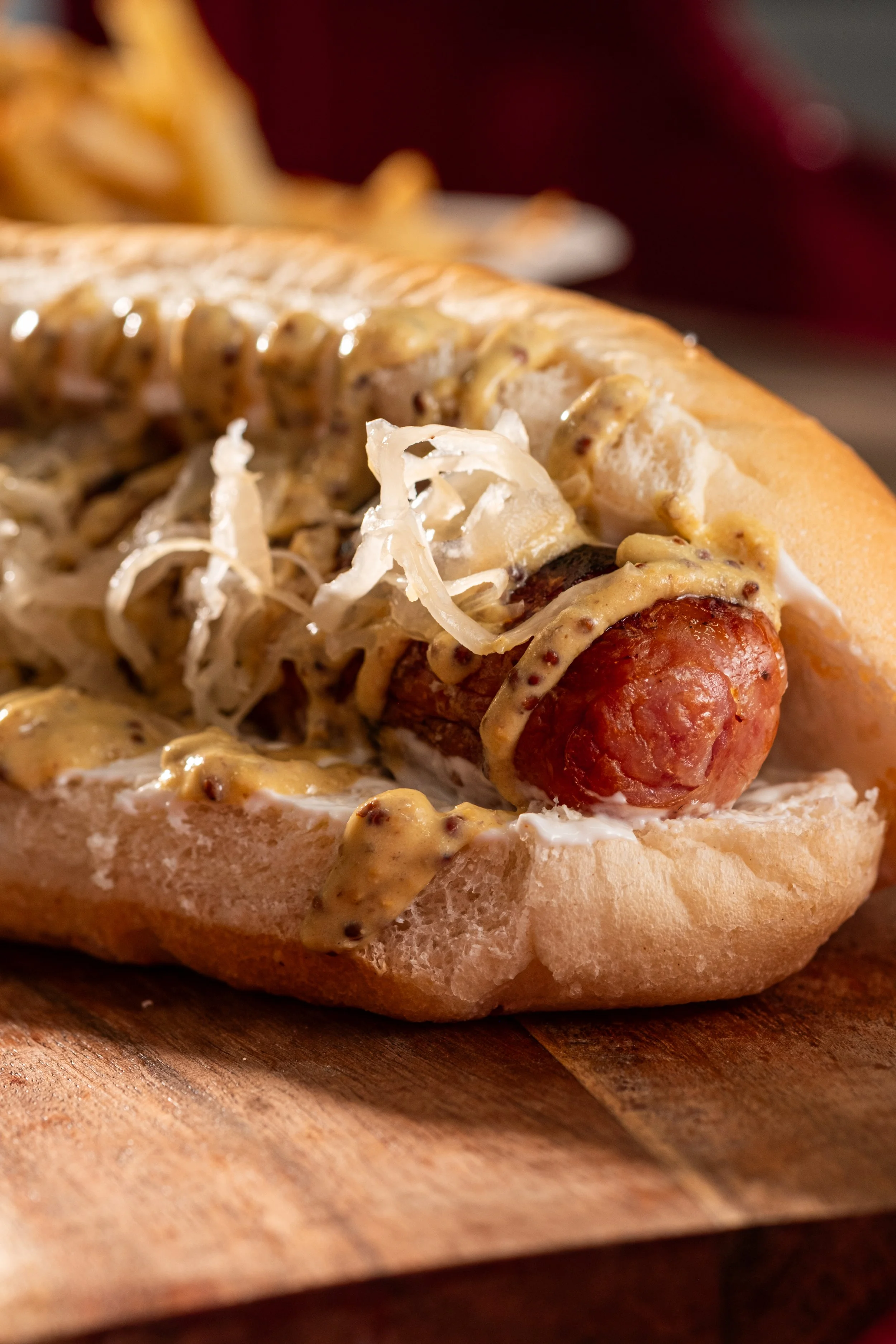 Close-up of hot dog in a bun topped with sauerkraut and mustard, on a wooden surface.