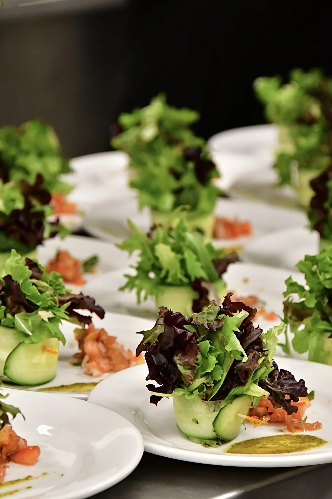 Multiple plates of innovative cucumber cup salads filled with colourful greens and topped with green dressing.
