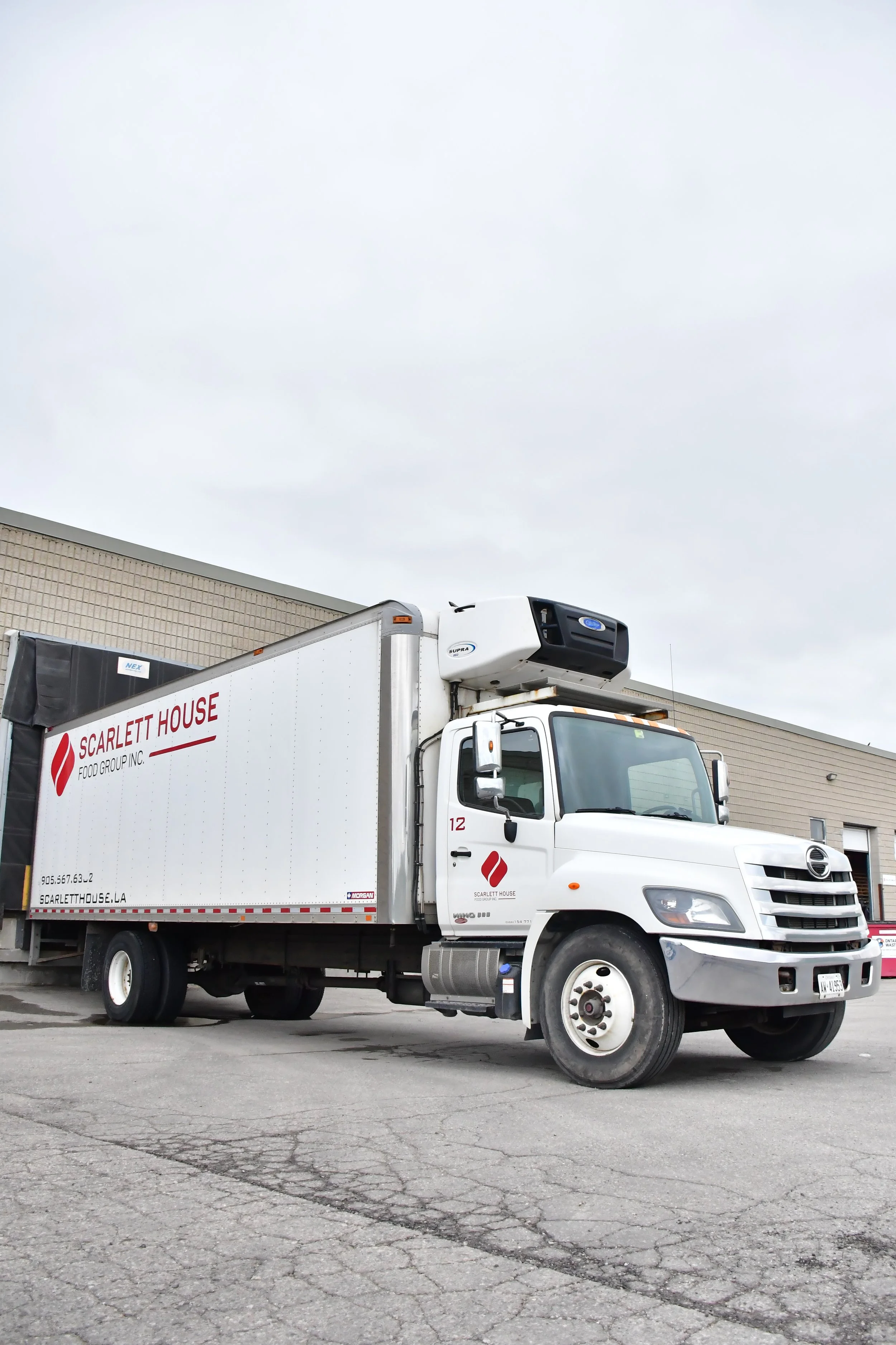 White delivery truck with Scarlett House Food Group Inc. logo parked in an industrial area under a cloudy sky.