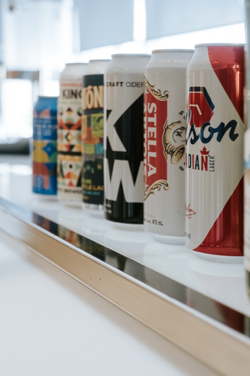 Line of various canned beverages on a white shelf.
