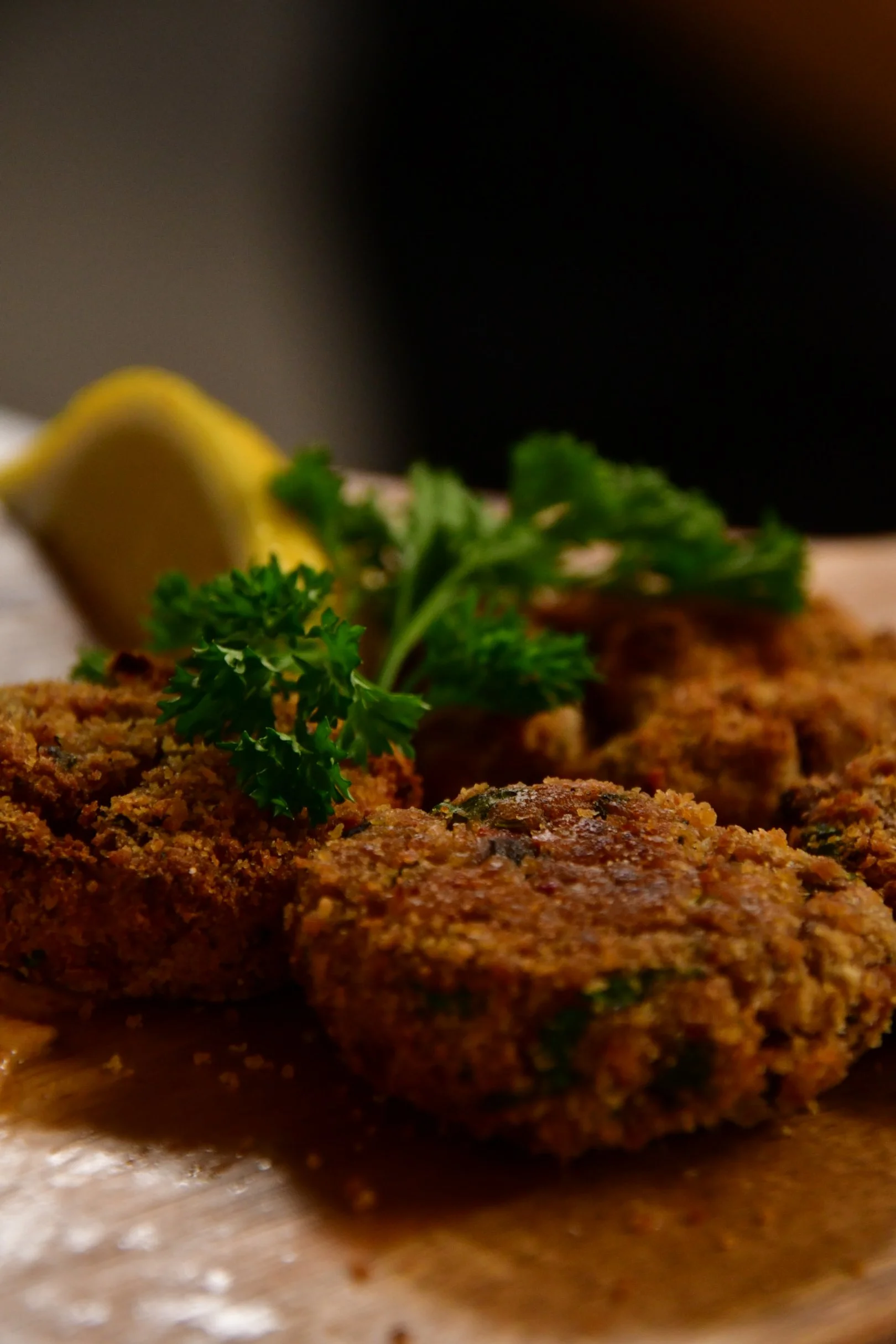 Close-up of crispy falafel garnished with parsley and lemon wedges on a wooden tray.