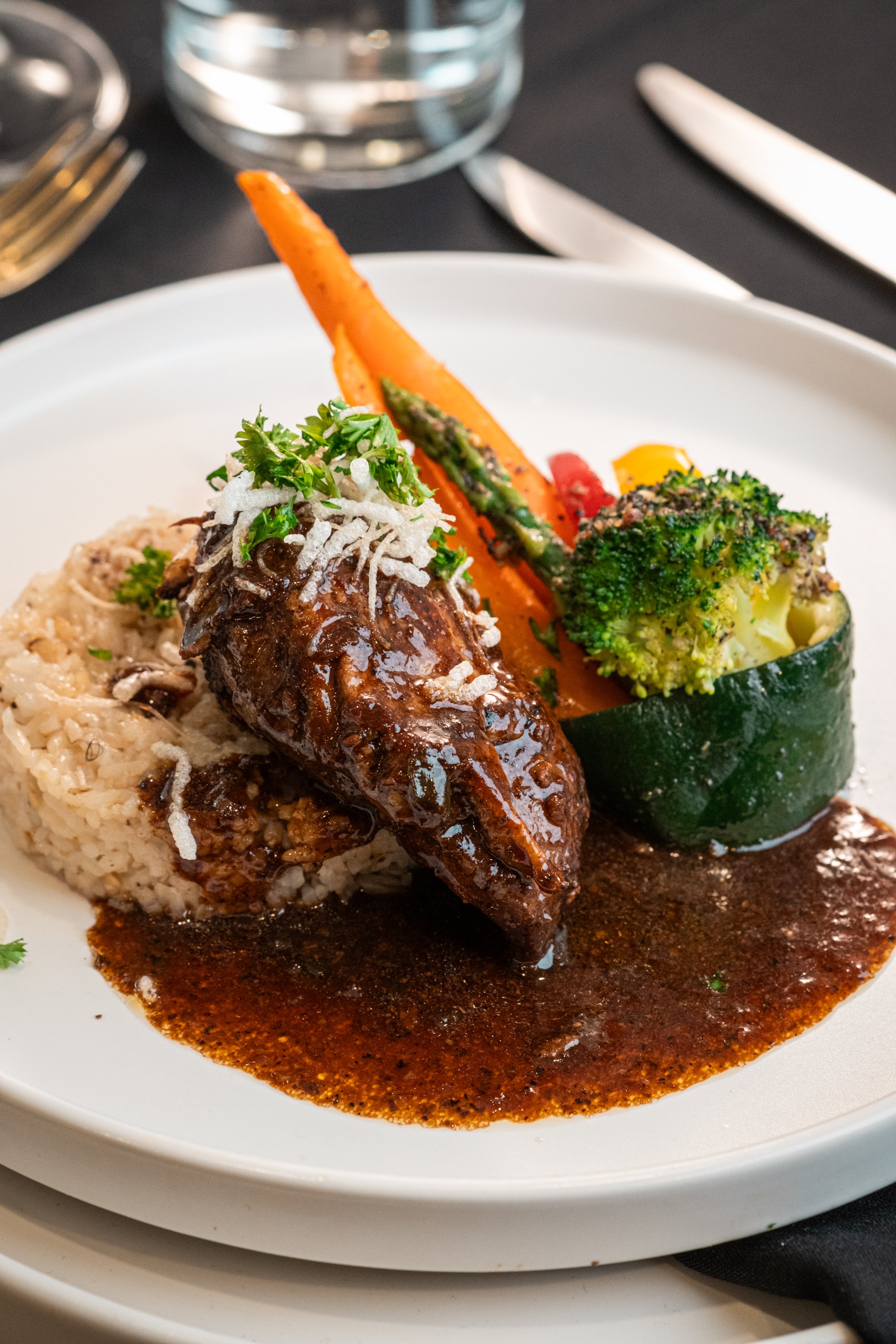 A plate of food featuring a large piece of meat topped with gravy, served alongside mashed potatoes with gravy, steamed broccoli, served with carrots, asparagus, and a roasted zucchini slice.