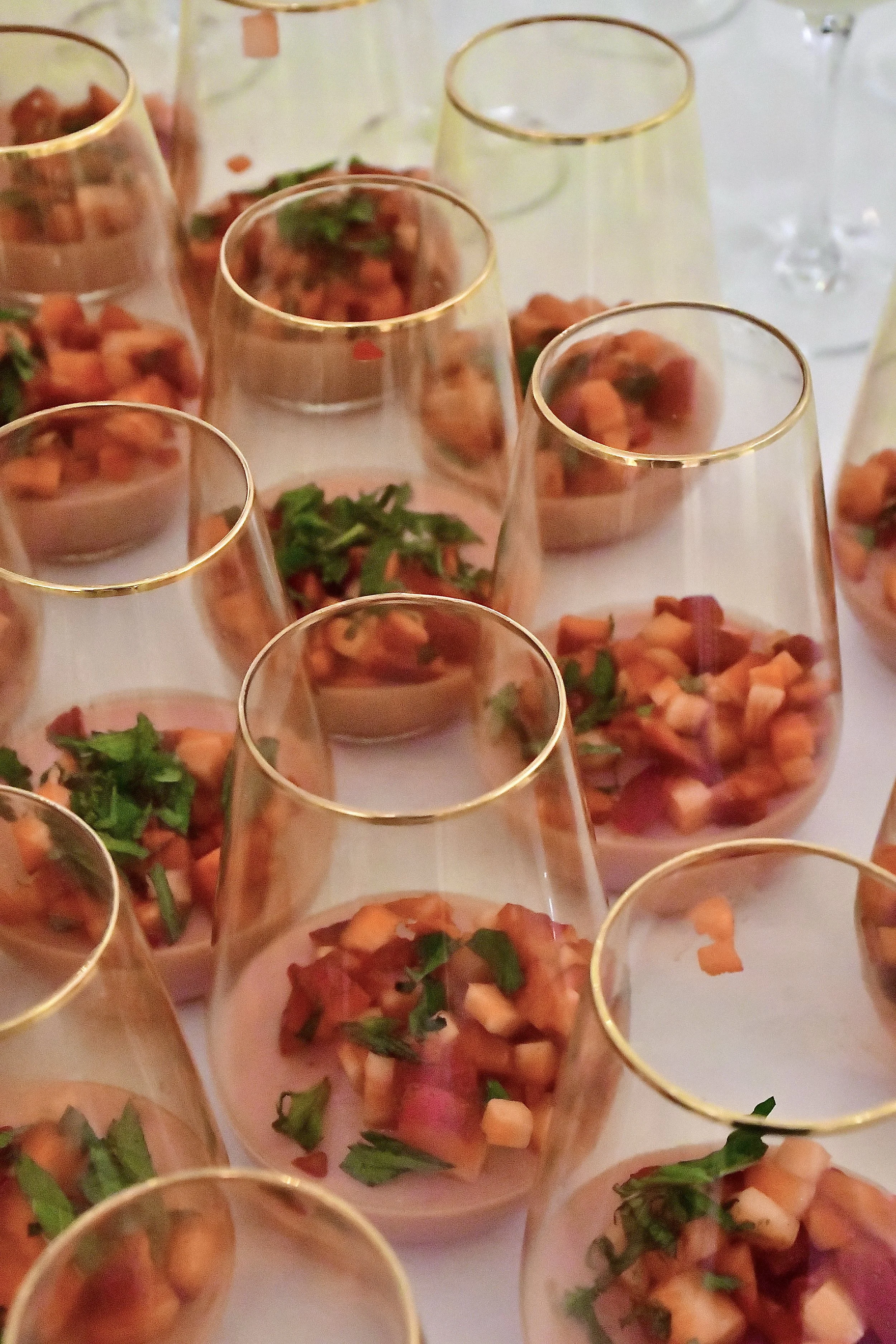 Multiple clear glasses with gold rims filled with strawberry panna cotta, diced strawberries and garnished with fresh chopped mint.