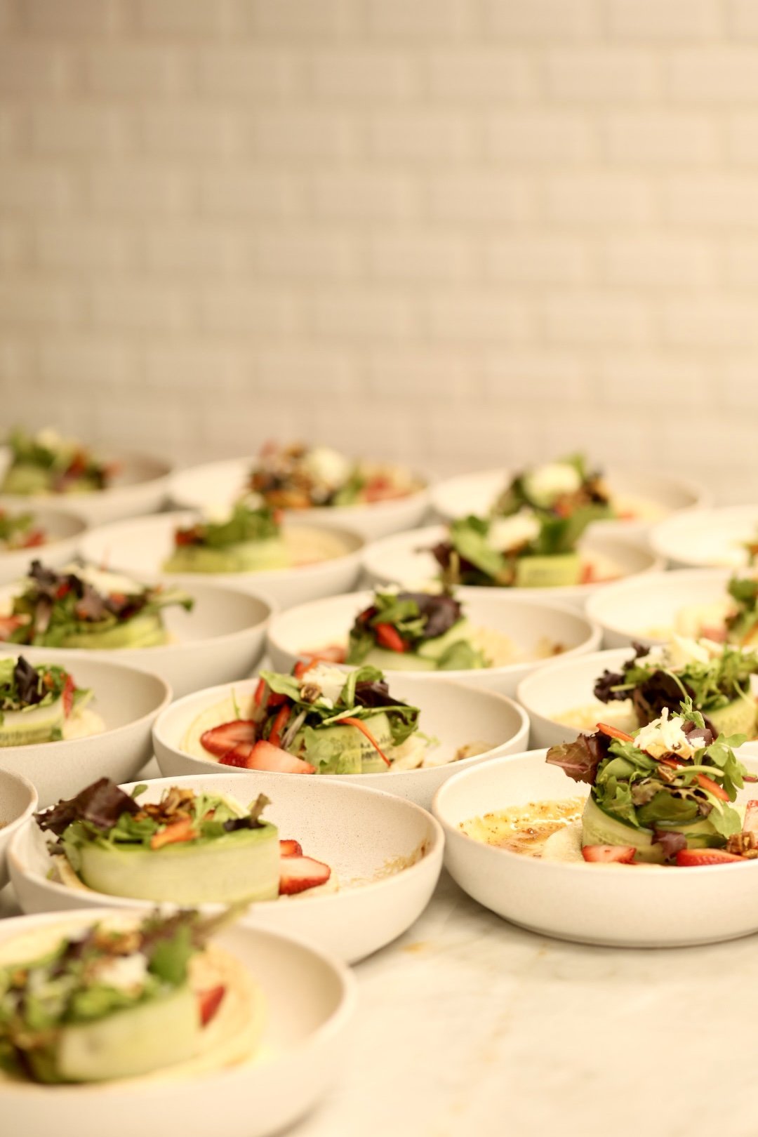 Multiple white bowls filled with salad, topped with sliced strawberries, mixed greens, and shredded vegetables, arranged on a marble surface.