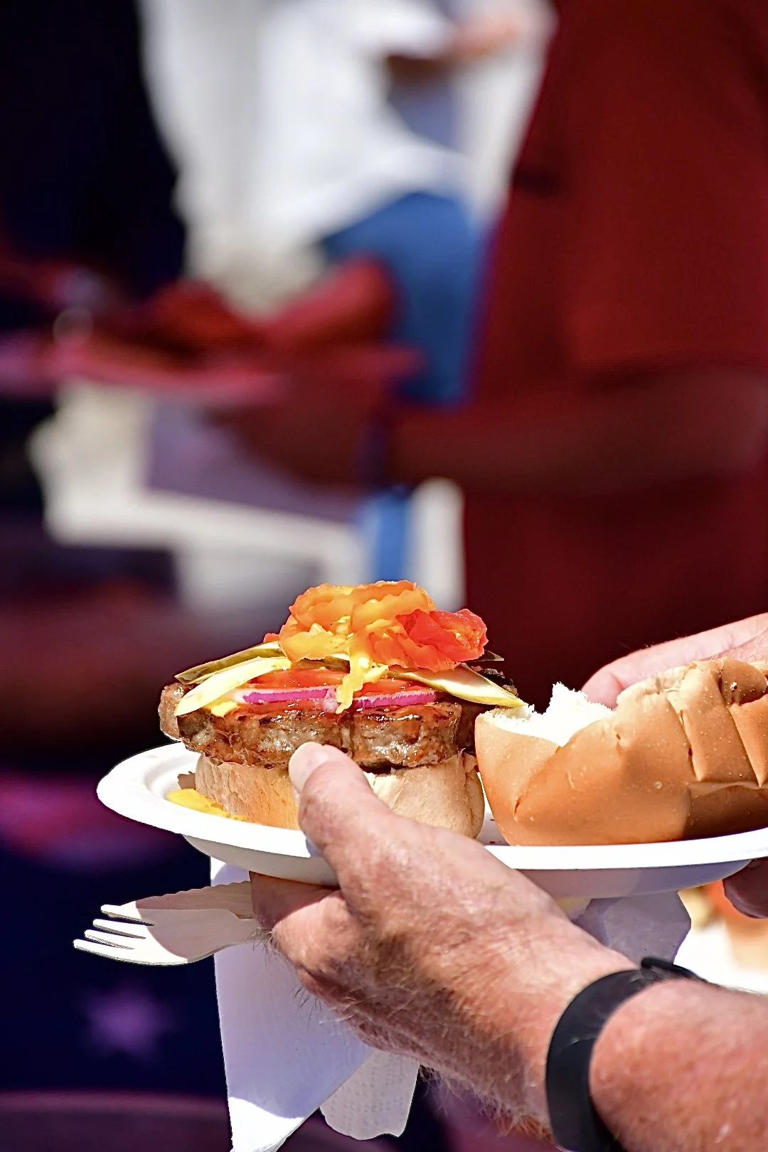 Close-up of a person holding a plate with a burger topped with banana peppers, and condiments.