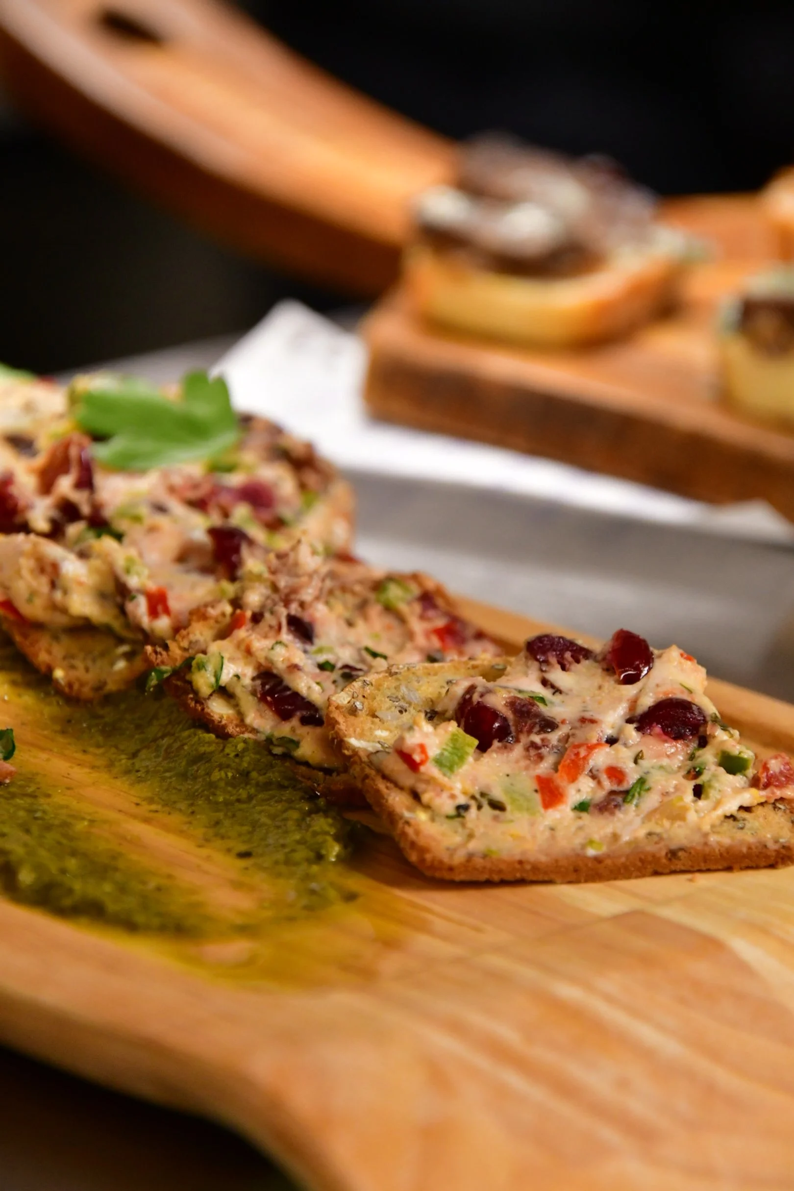Olive tapenade on a toasted crostini served on a board with green sauce garnish.