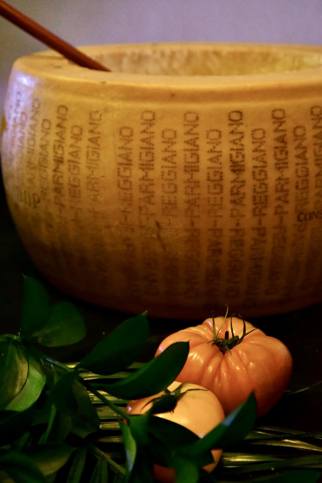 A large wheel of parmesan hollowed out for tossing pasta in with some greenery and fresh heirloom tomatoes for table decor.