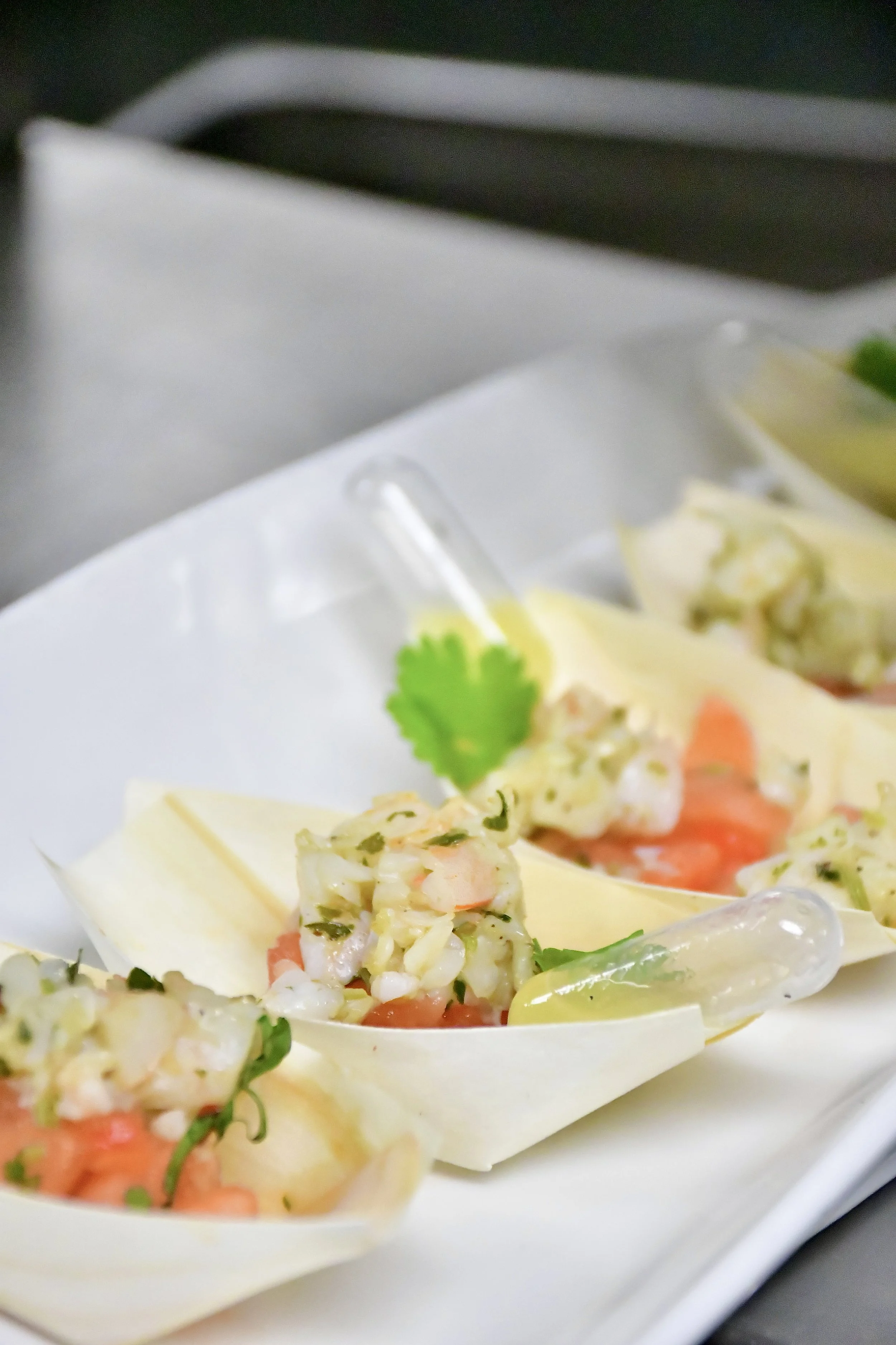 Close-up of seafood appetizer in wooden serving boats with individual lemon juice squeeze capsules, garnished with a cilantro leaf.