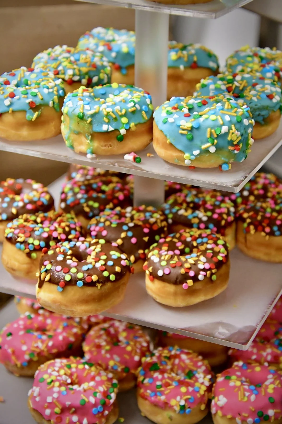 Display of colorful donuts with various frostings and rainbow sprinkles on a multi-tiered stand
