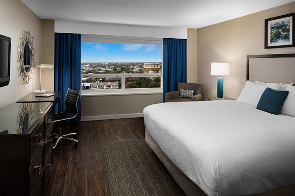 hotel guestroom with one king bed and a view of the city from an open window