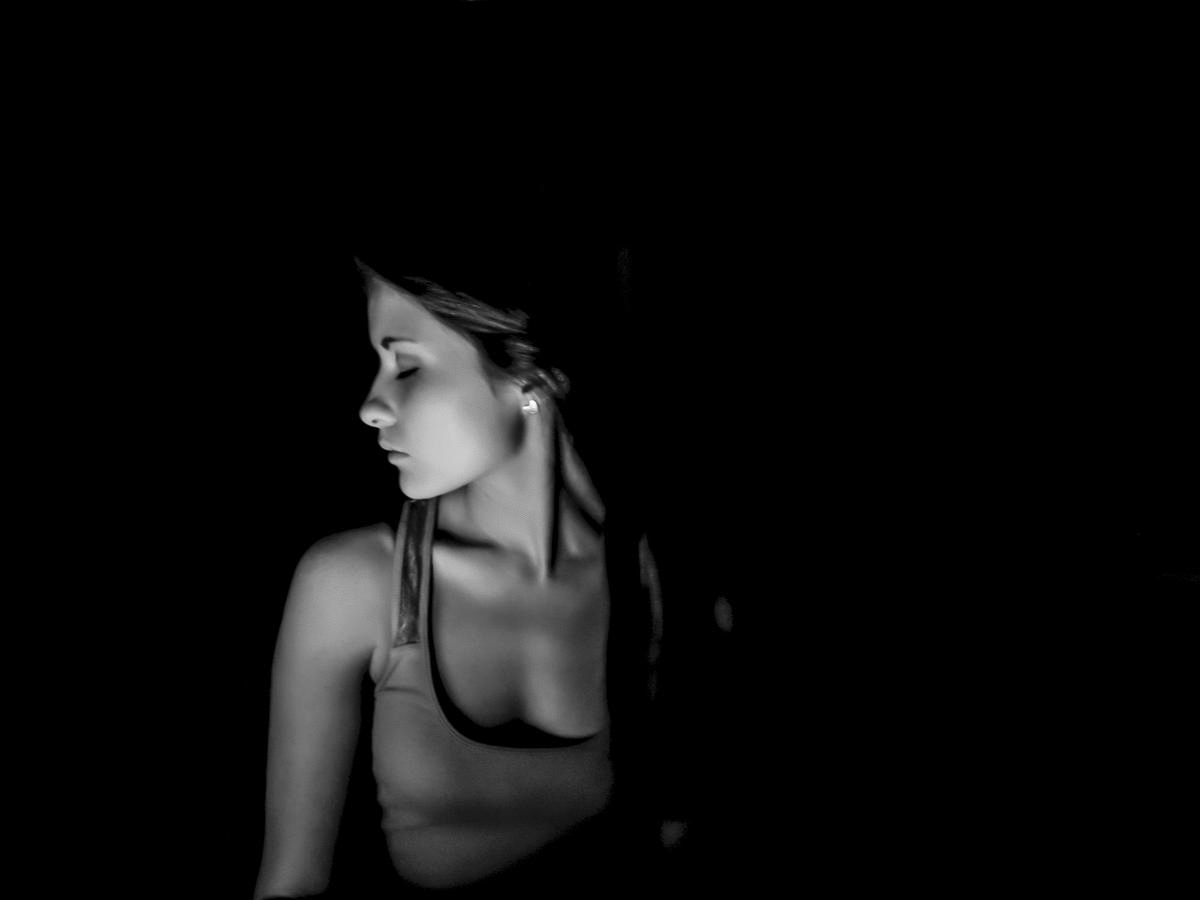 Black and white photo of a young woman with long hair, closed eyes, and a relaxed expression, facing left in a dark setting.