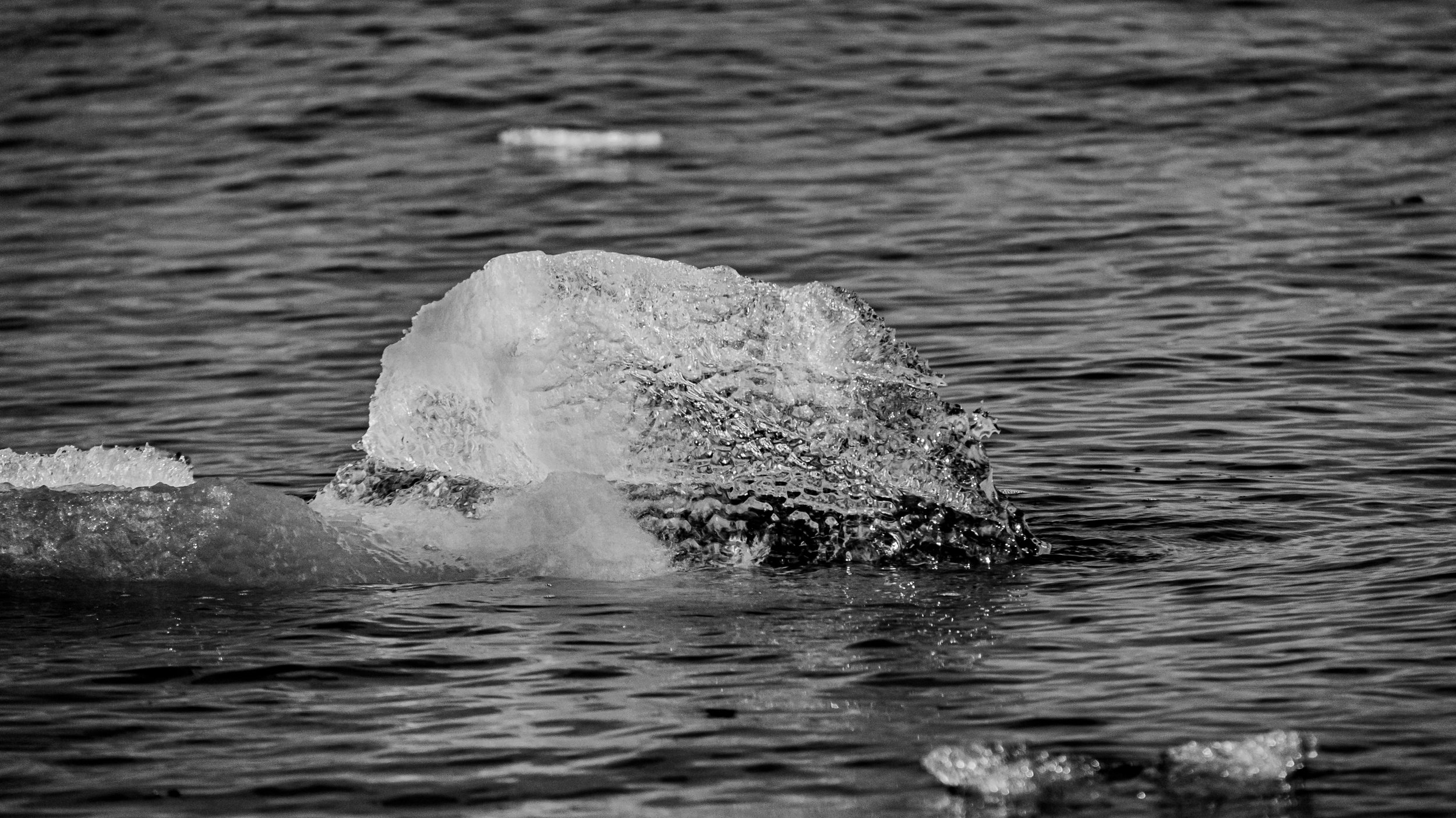 A large chunk of ice floating in a body of water, with smaller ice pieces nearby, in black and white.